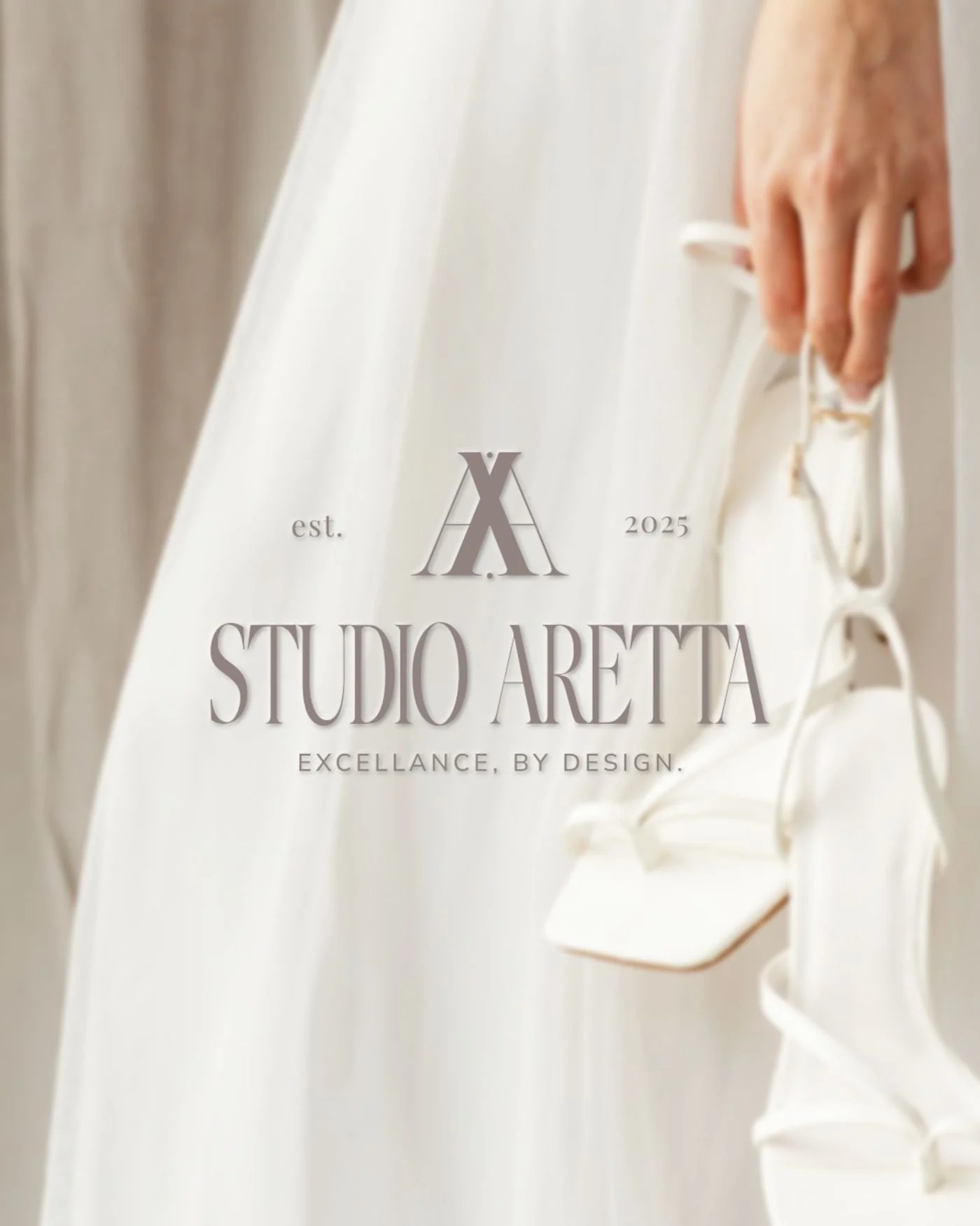 Close-up of a woman in a white dress holding a pair of white high-heeled shoes with the text 'Studio Aretta, est. 2025, excellence by design' overlaid.