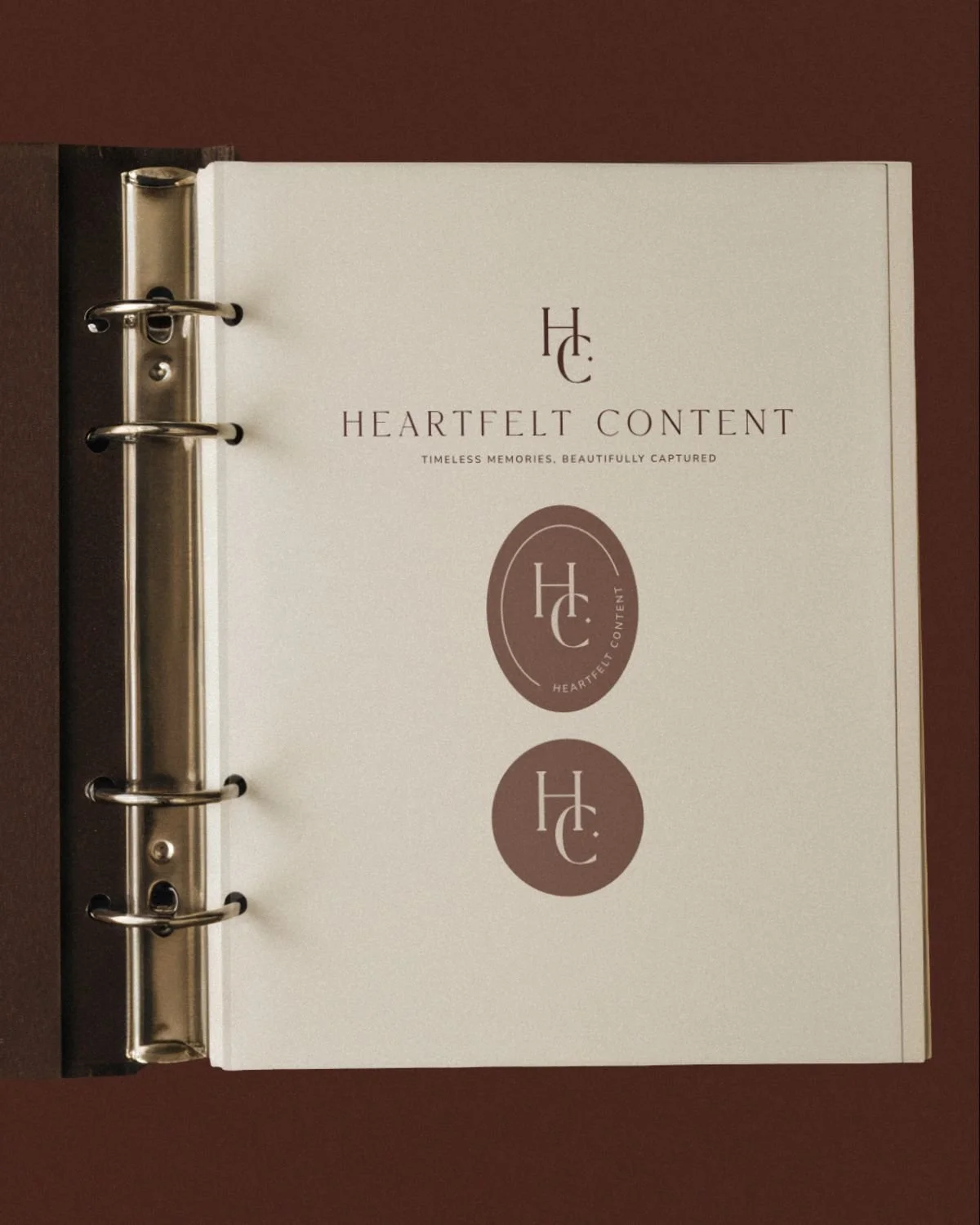 An open ring binder showing the Heartfelt Content brand guidelines page with the HC monogram logo in two variations