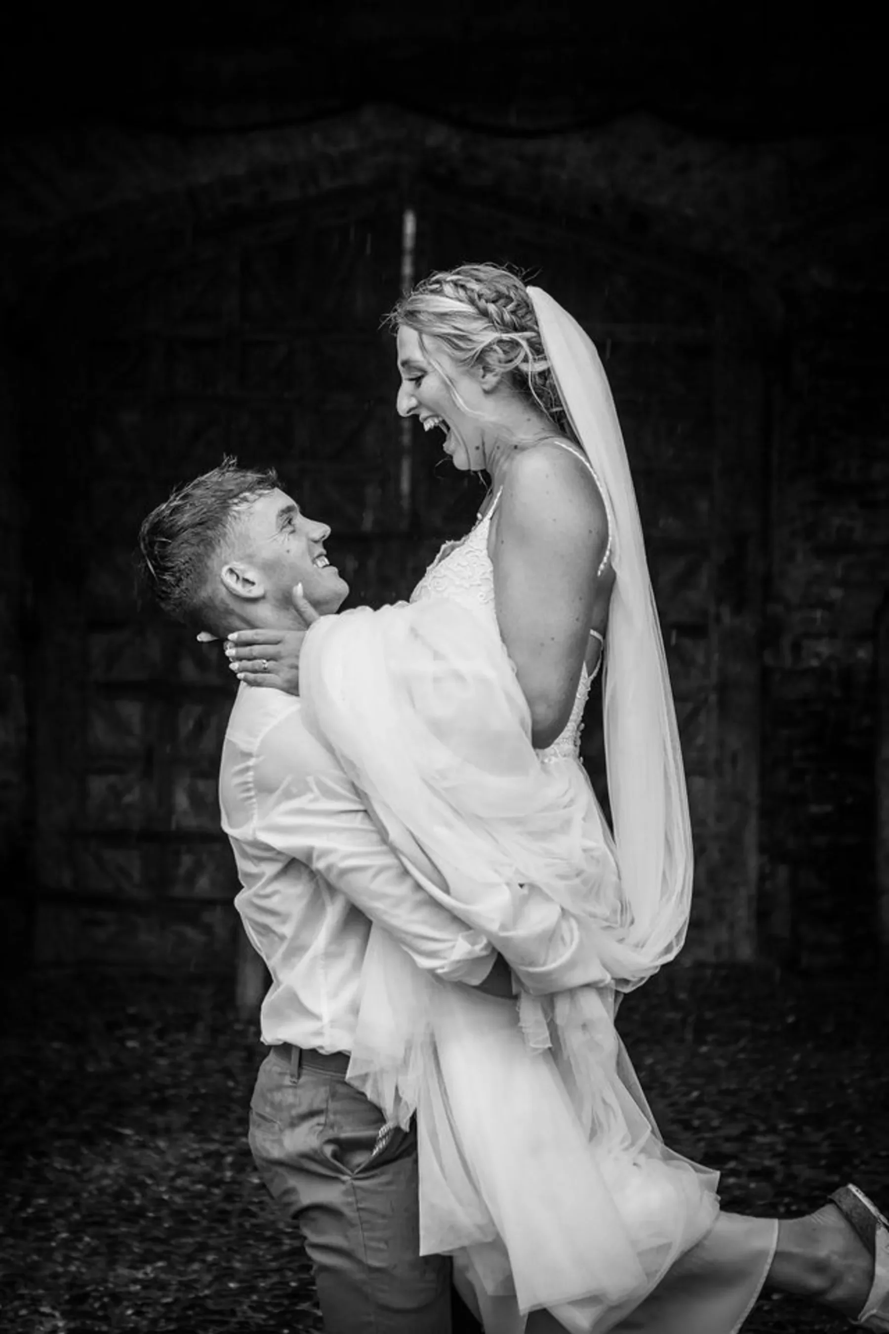 A groom lifts a laughing bride in her veil; both radiate joy—perfect for wedding photographer branding in black and white.