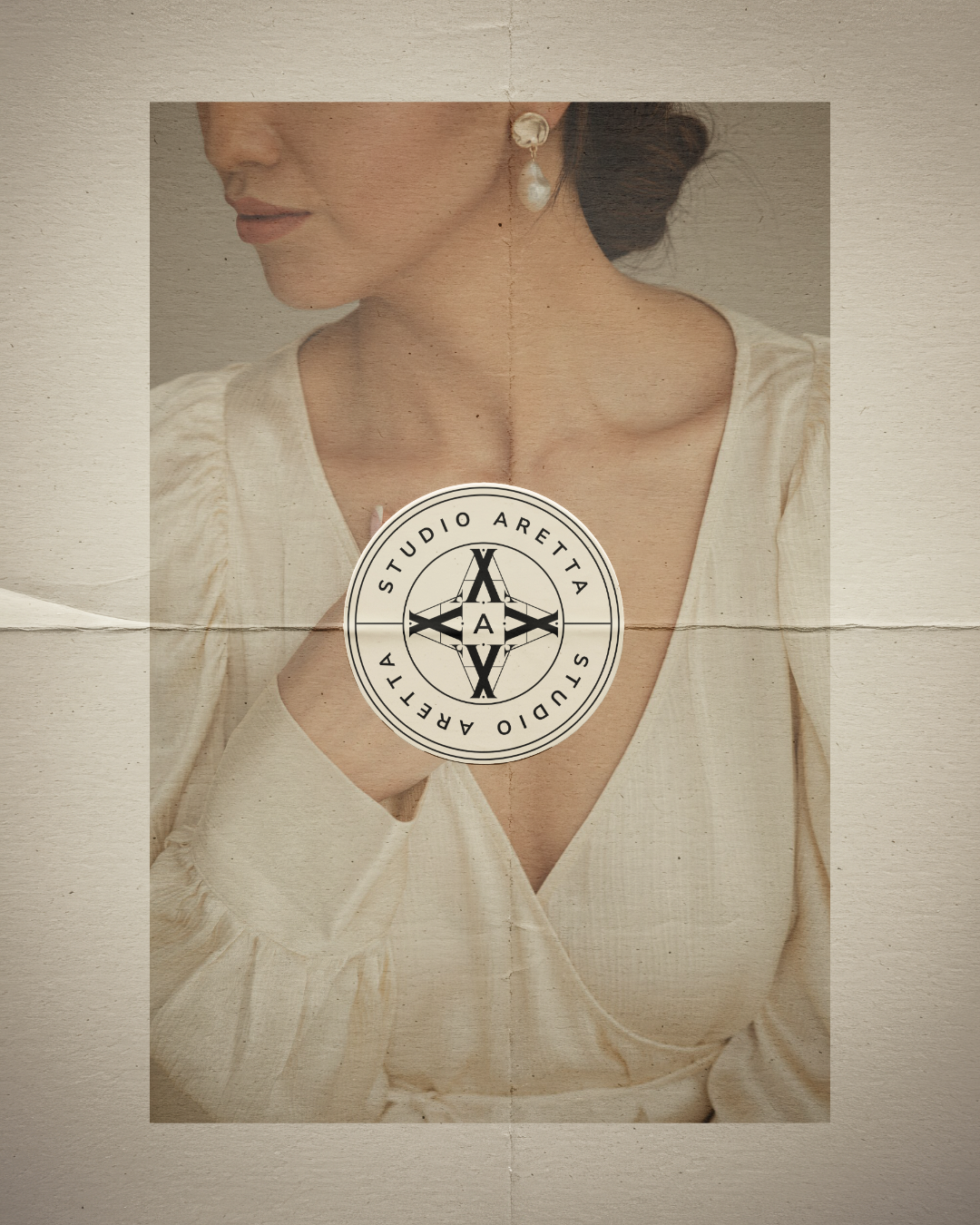 A woman wearing pearl earrings and a cream-colored blouse with a deep neckline. Her face is partially visible, turned slightly to the side. There is a circular logo overlay in the center with the text 'Studio Aretta' around it.