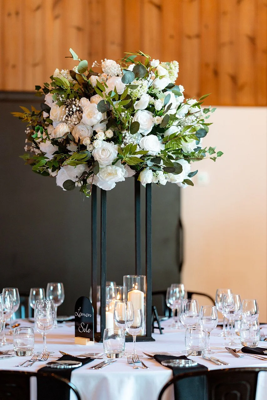Tall floral centerpiece with white roses and eucalyptus on a dinner table, featuring a place card for Lemon Sole.