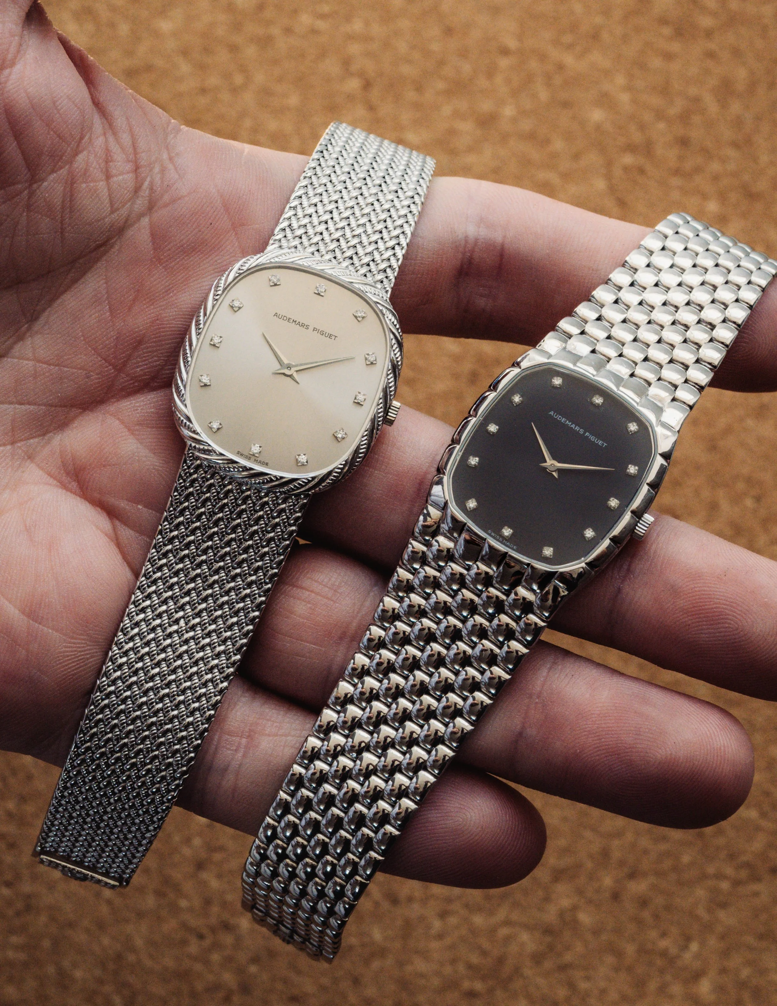 Close-up of three wristwatches with metal bands, held in a person's hand against a wooden surface background.