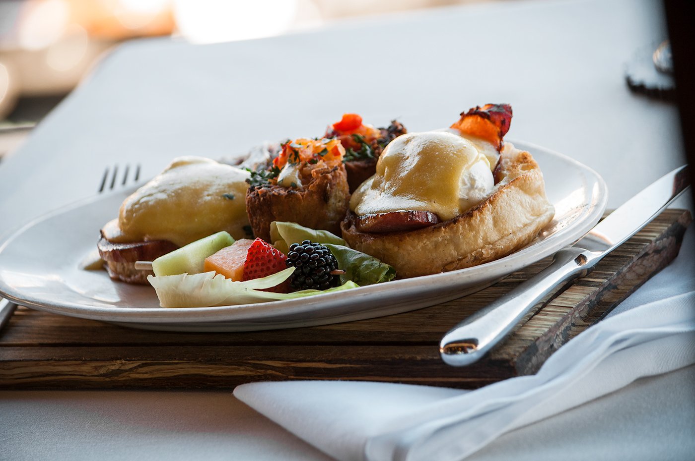 Plate of eggs benedict with fruits and vegetables at a restaurant table.