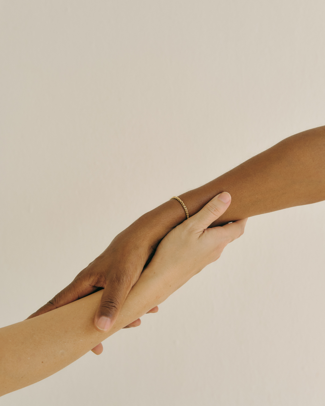 Two hands holding each other's arms, one with a gold ring on the finger, against a plain beige background.
