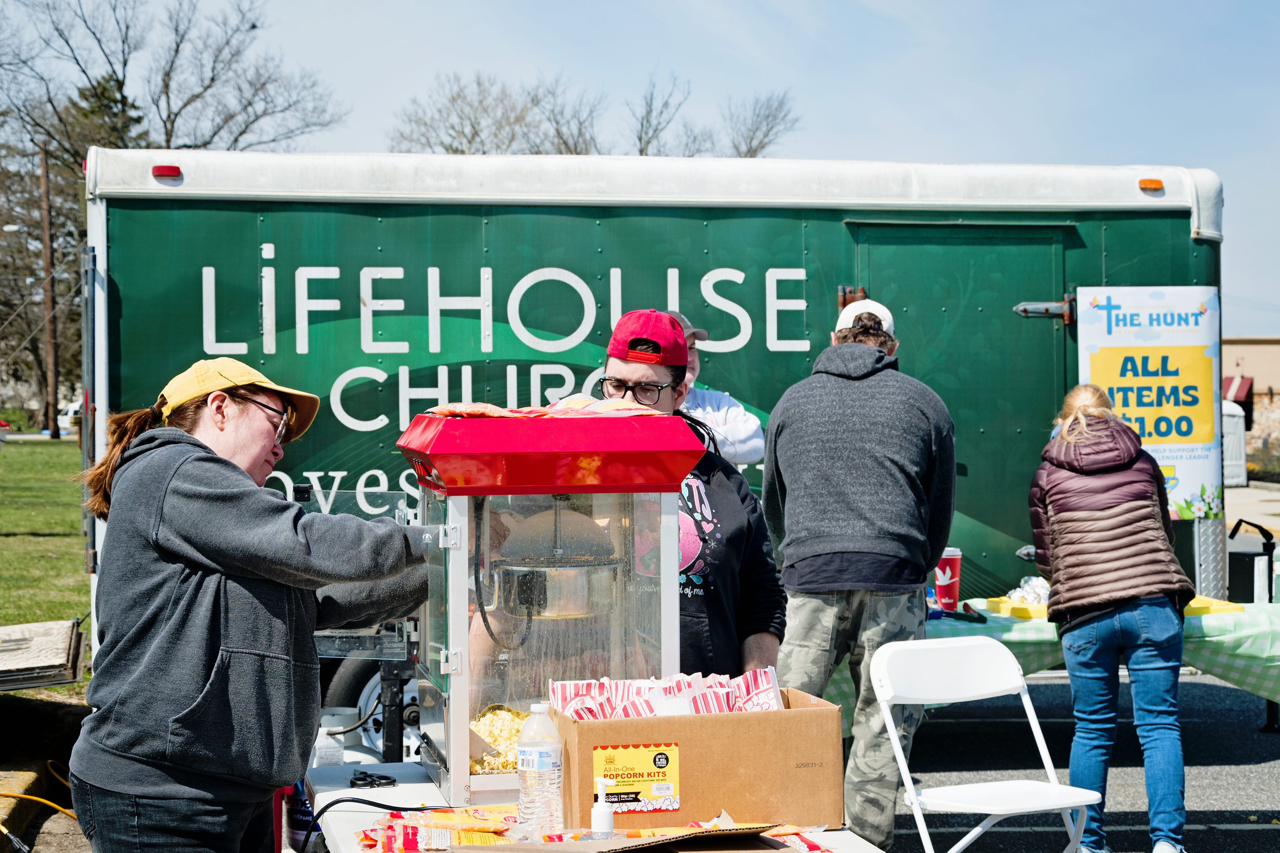 People at a community event with a green truck in the background, serving food and snacks at the table.