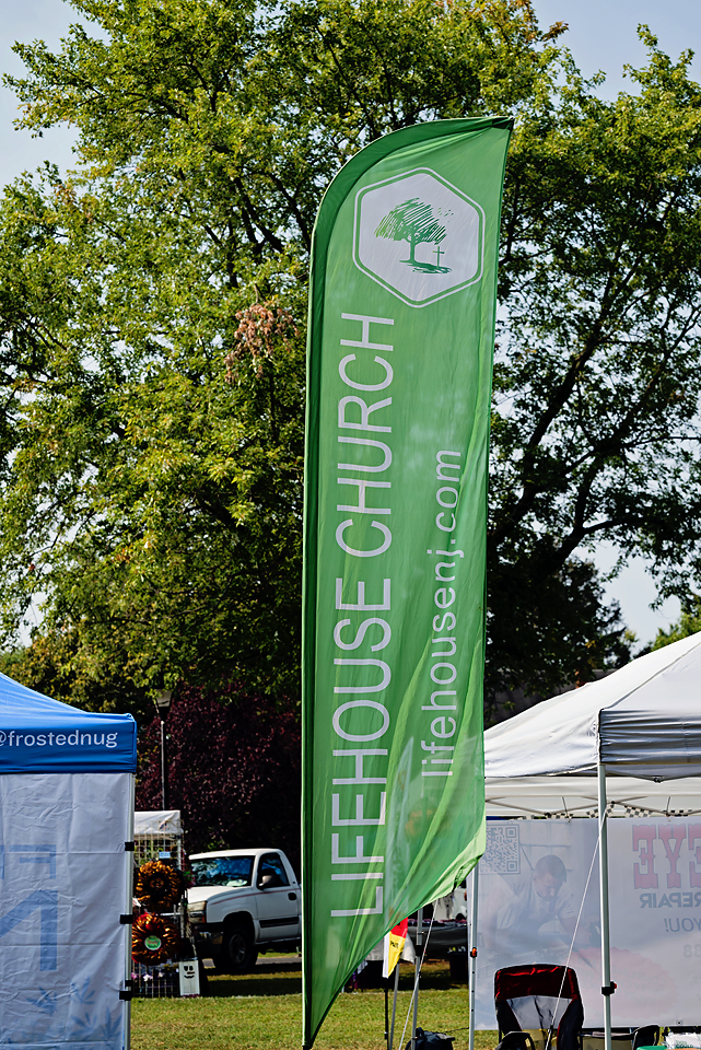 Tall green banner with the logo and URL for Lifehouse Church, with tents and a vehicle in the background.