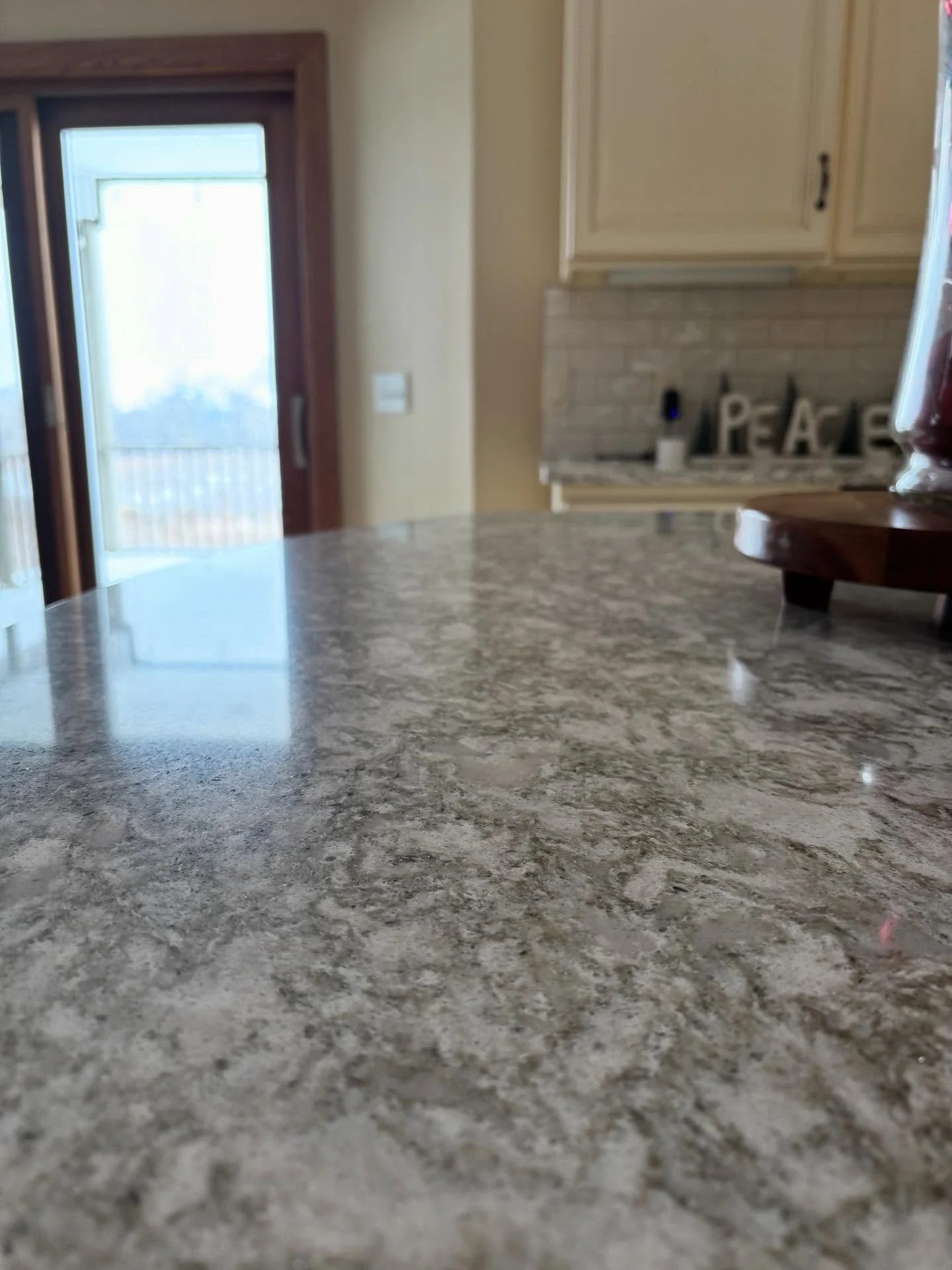 Close-up view of a granite kitchen countertop with a blurred background of a sliding glass door and kitchen cabinets.