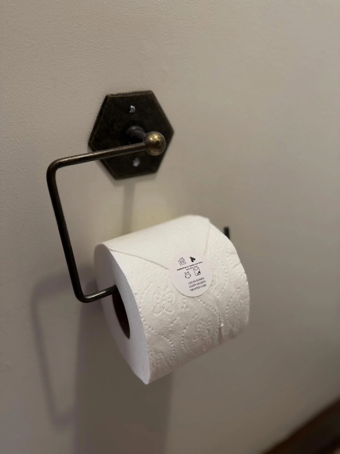 Toilet paper roll on a wall-mounted holder with a sticker that reads 'Clean homes, happy hearts, trusted care'.