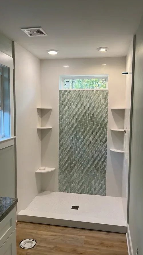 Open-concept grout-free porcelain shower with mosaic tile accent wall and built-in corner shelves in Michigan bathroom