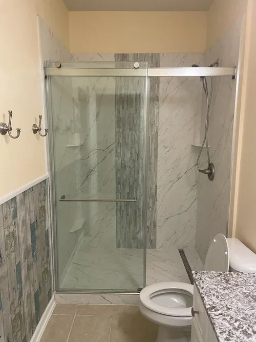 Full bathroom view of white marble porcelain shower with gray wood-look accent wall and chrome sliding door in Michigan home