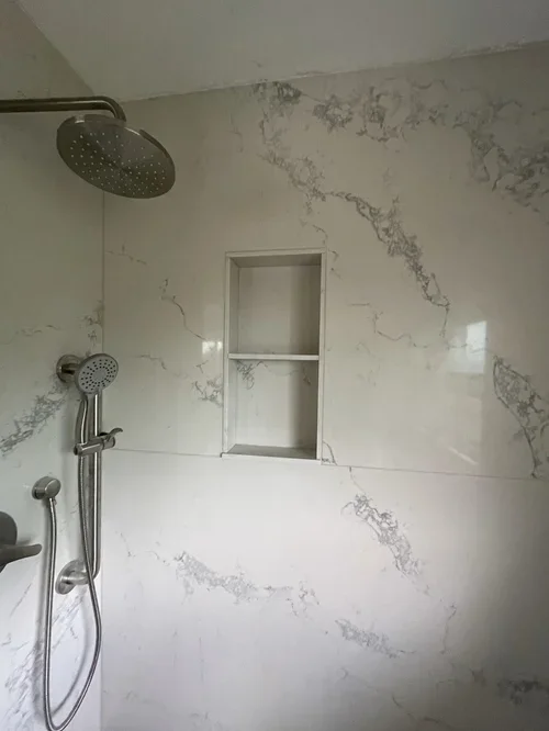Close-up of seamless white marble porcelain shower corner with built-in niche and rain showerhead in Michigan bathroom
