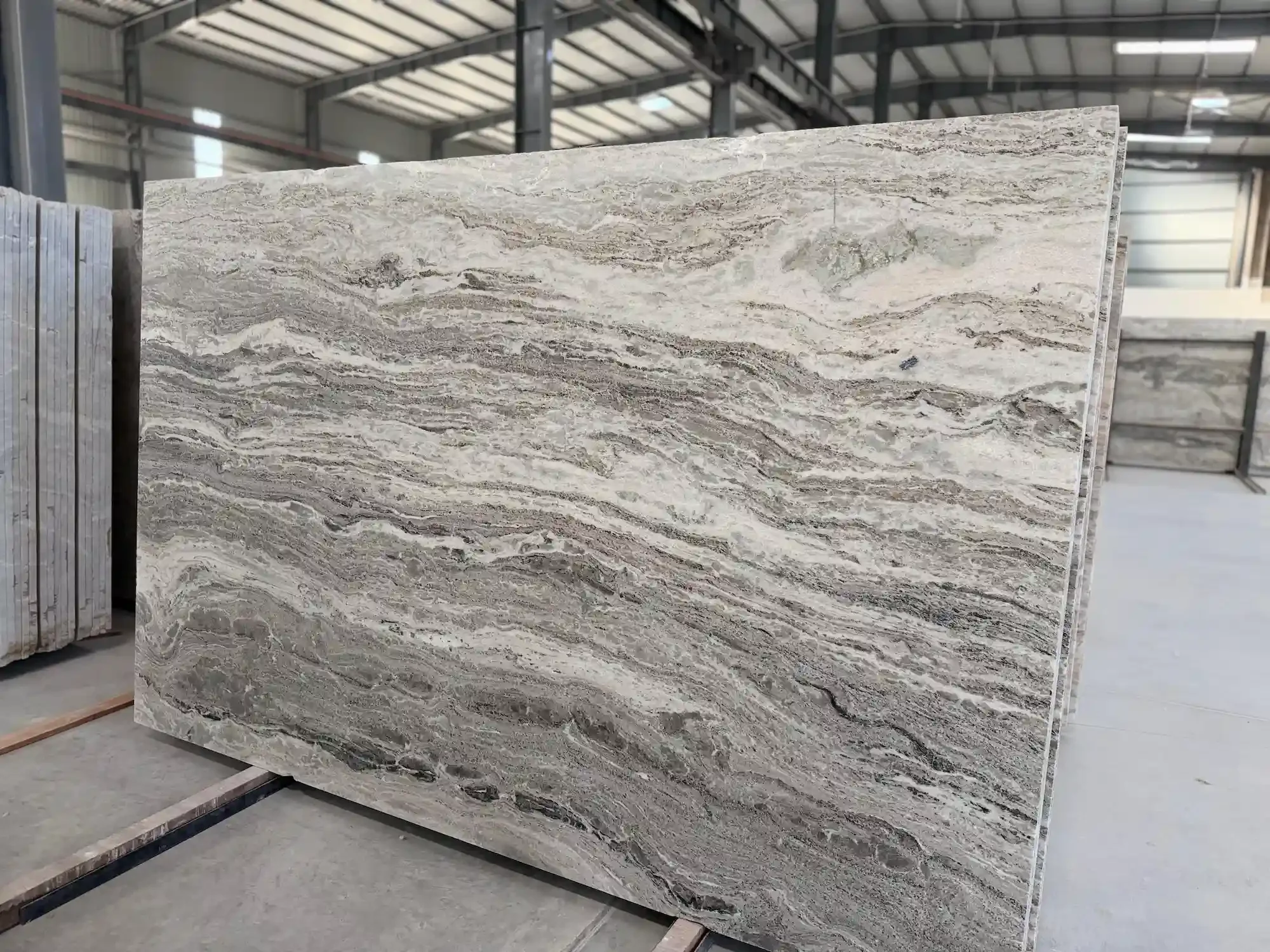 Detail of Fantasy Brown stone slab showing dramatic diagonal waves of grey, apricot, and white. Patterned natural stone perfect for waterfall kitchen islands.