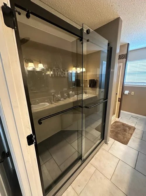 Grout-free porcelain shower with beige walls and black sliding glass door installed in Michigan bathroom