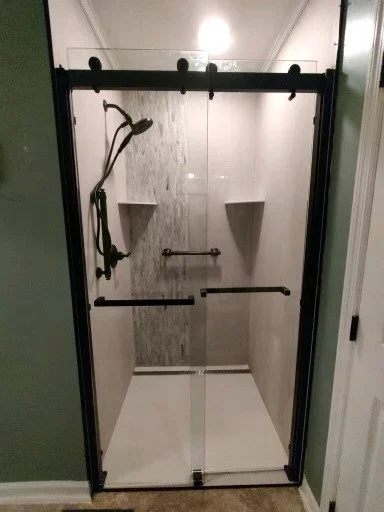 Modern grout-free porcelain shower with gray wood-look accent wall and black sliding door installed in Michigan