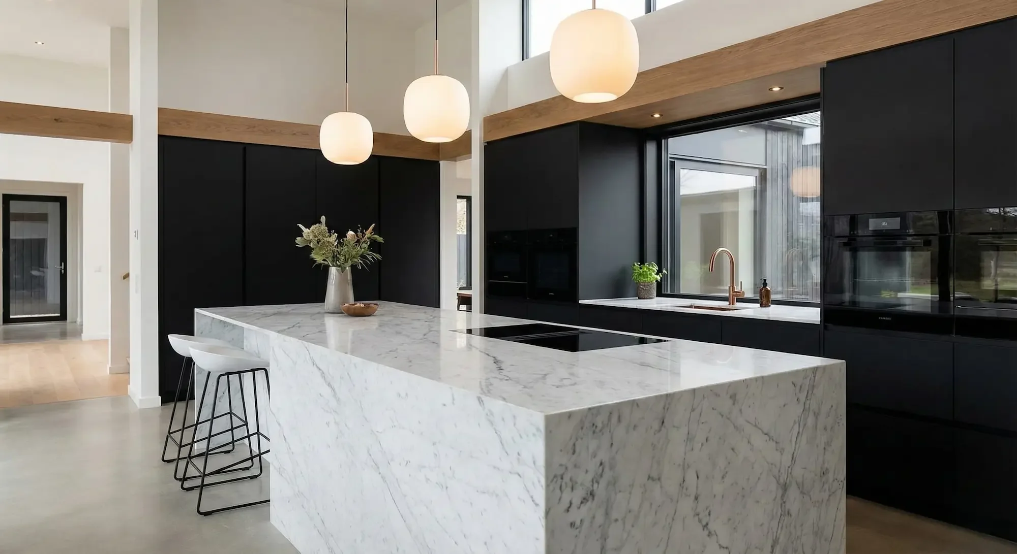 Modern kitchen with white marble island, black cabinetry, wooden accents, and large window.