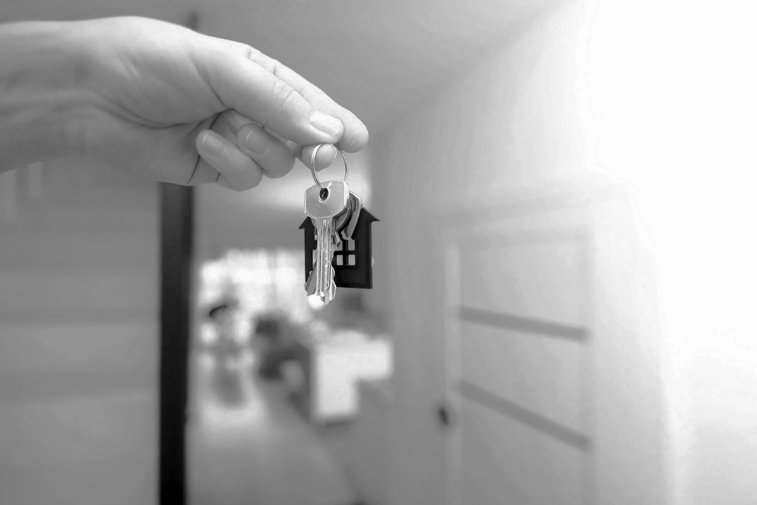A hand holding a keychain with keys and a small house-shaped keychain in front of school lockers.