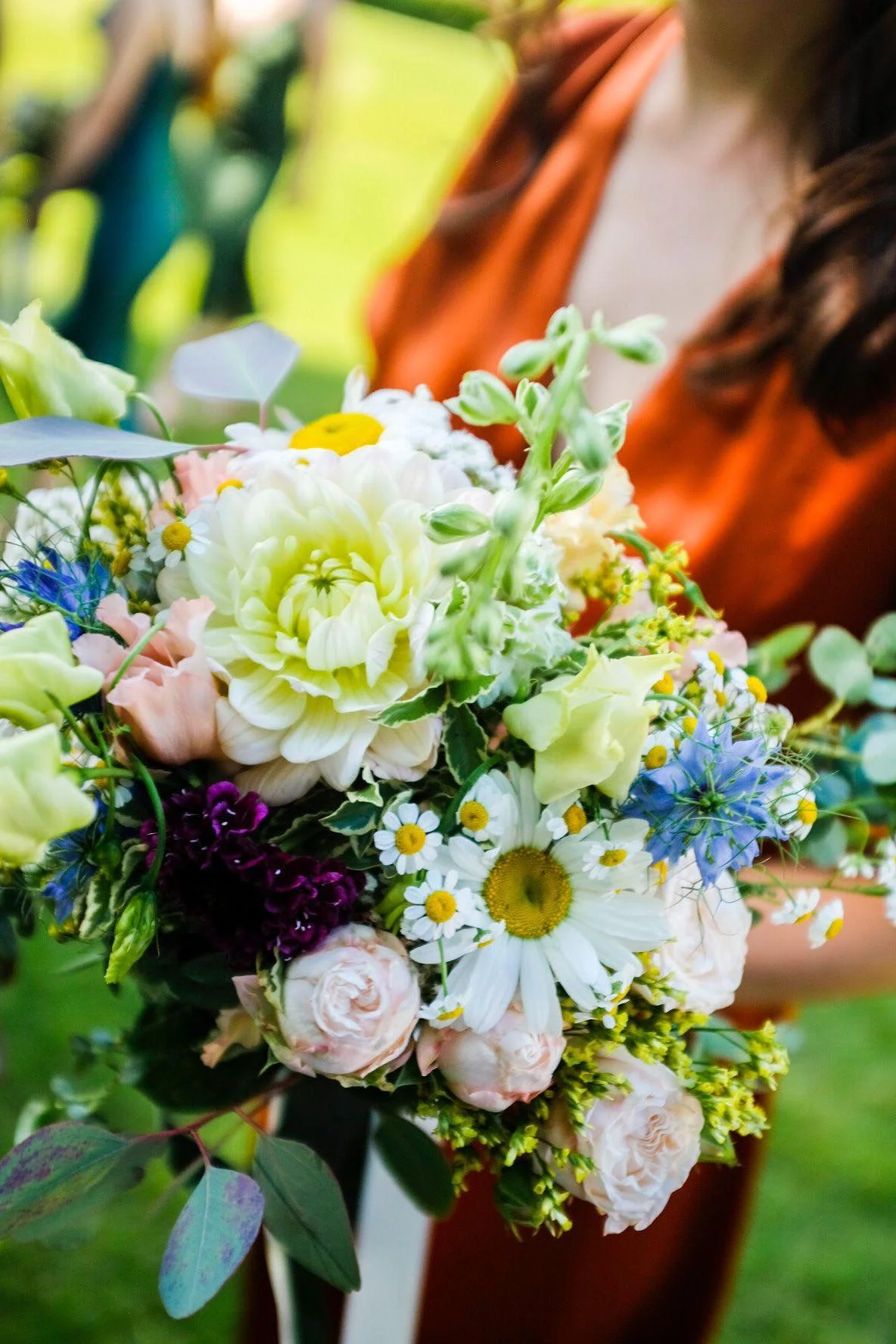 A person holding a colorful bouquet of various flowers, including daisies, roses, and other wildflowers, outdoors.
