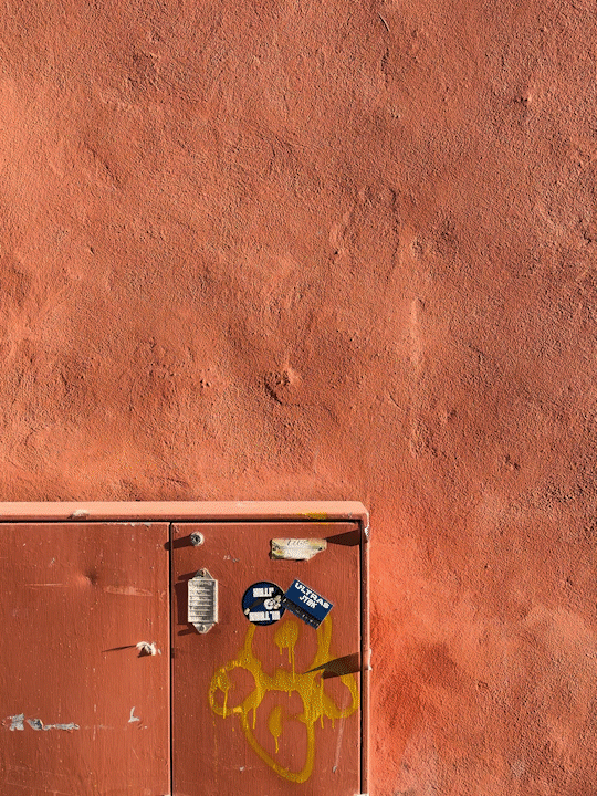 En orangebrun vägg, där Be & Arbetas nya produkt "Tygkasse Monstera" dyker upp när en person i rutig kavaj går framför väggen.