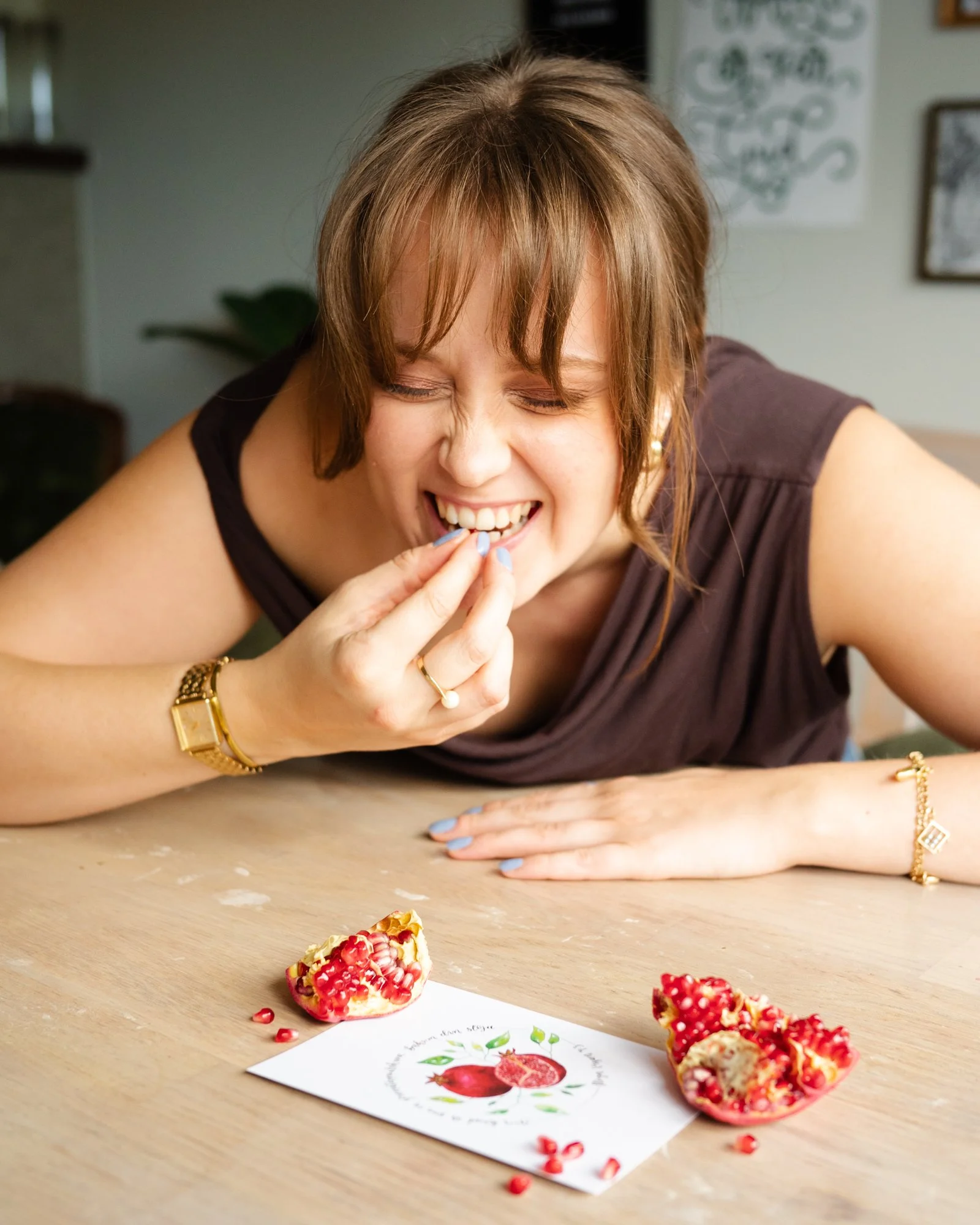 Glad kvinna ler och äter granatäpple framför ett pappret med ett vykort med motivet "Granatäpple".