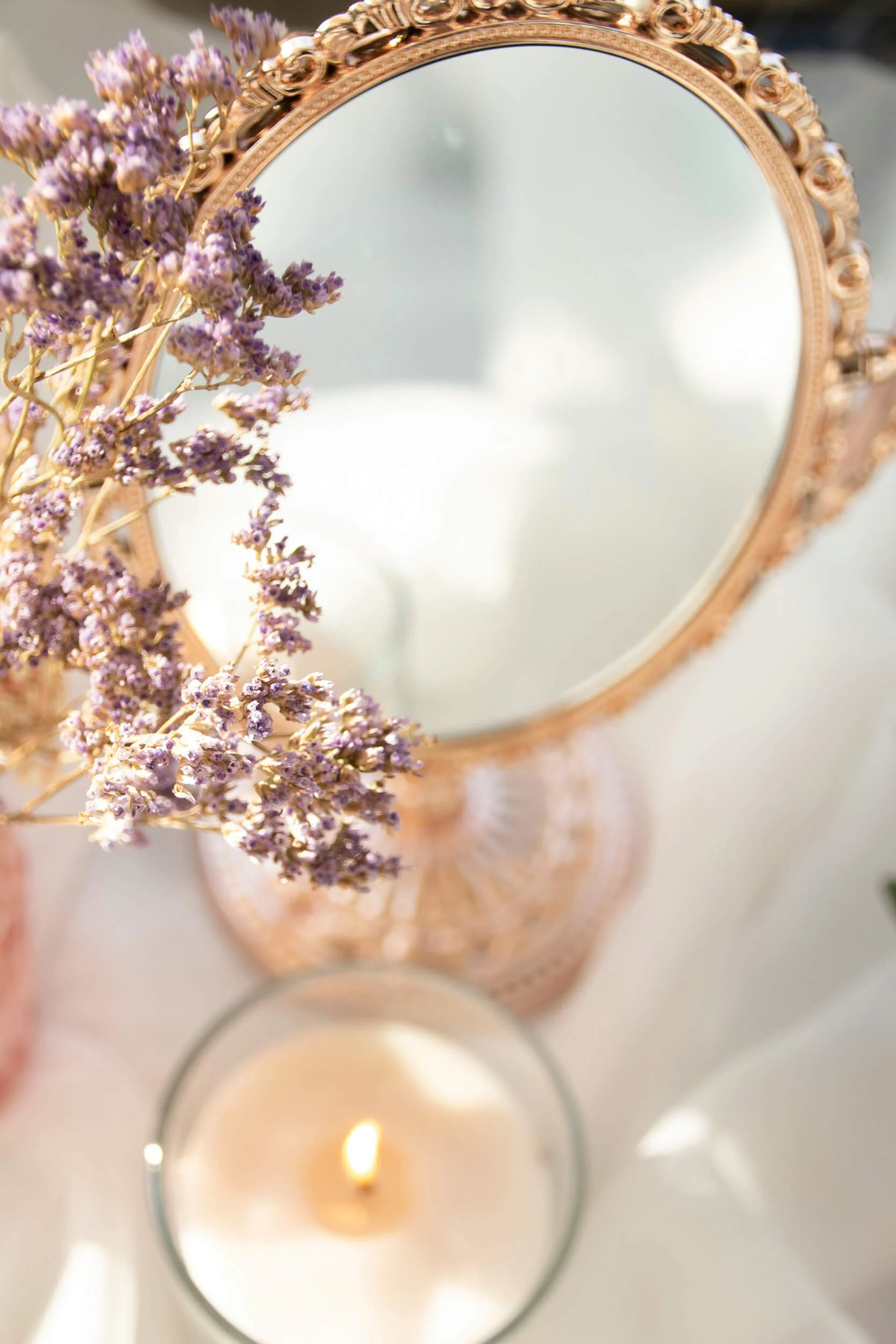 A close-up of a decorative mirror with a gold ornate frame and a bunch of dried purple flowers representing massage therapy in Chesterfield, VA.