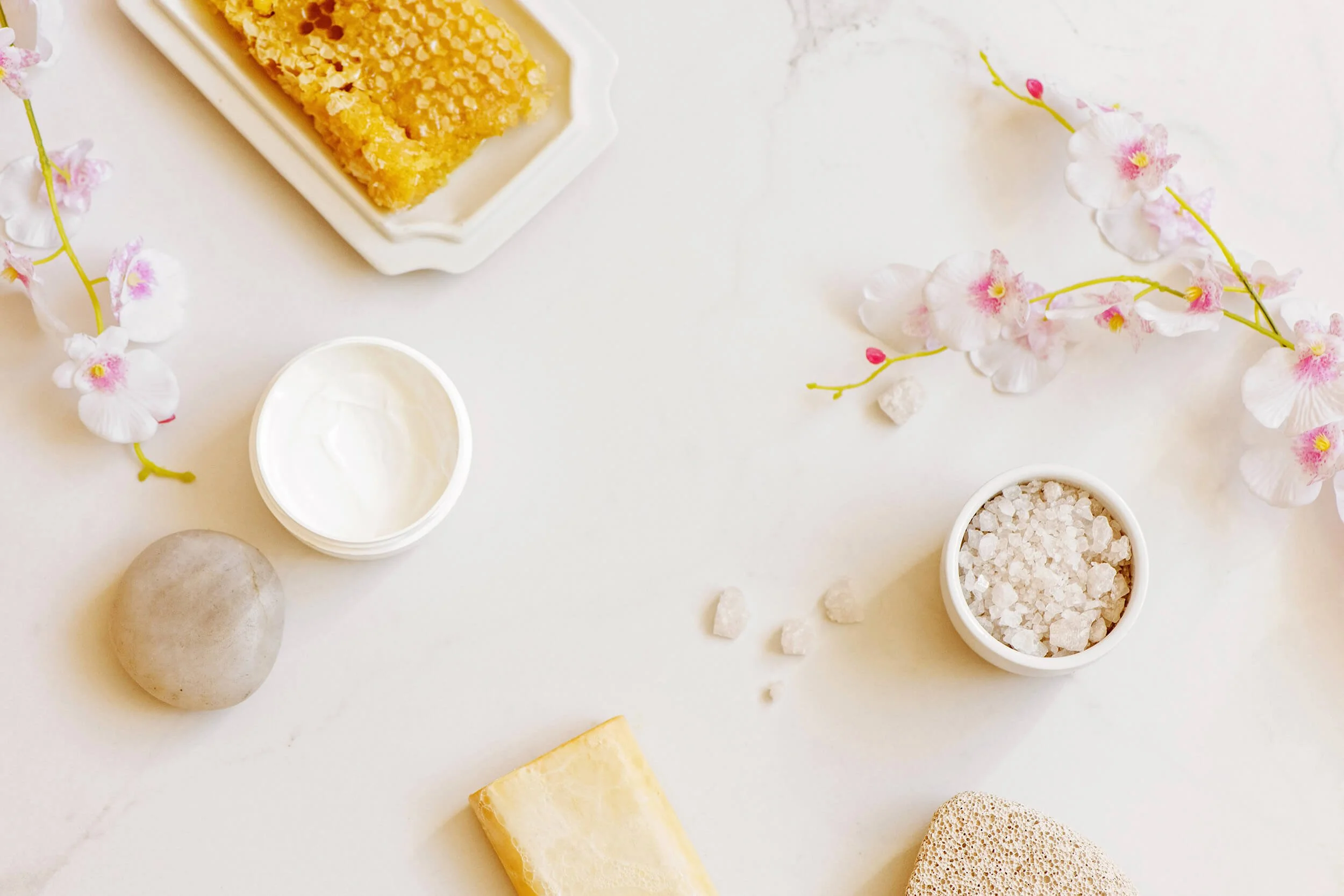Assorted natural ingredients and objects on a white surface, including honeycomb, cream, sea salt, a yellow soap bar, and a pumice stone representing massage therapy in Chesterfield, VA.