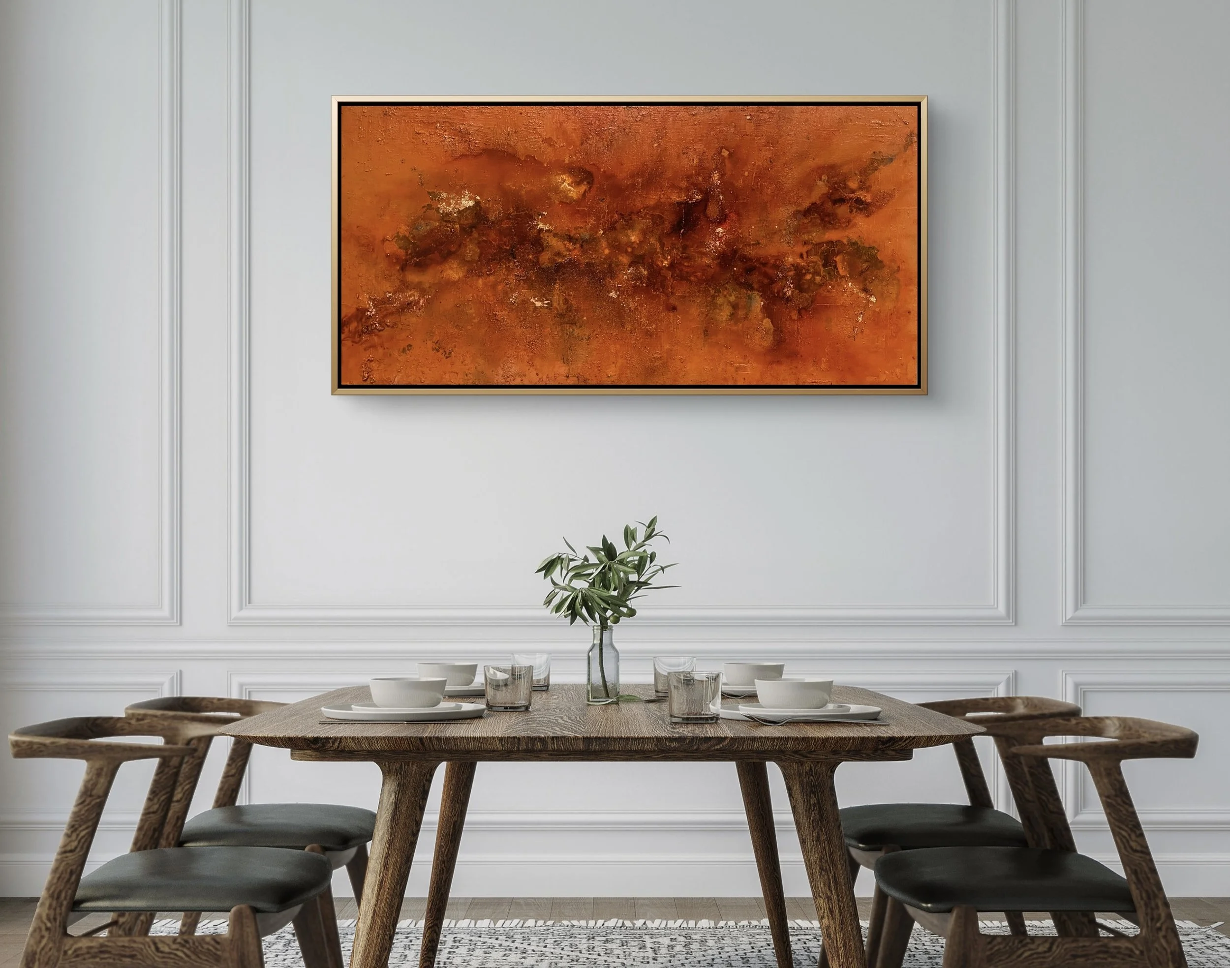 A dining room with a wooden table set with white bowls, glasses, and a vase with green leaves, against a white wall with decorative paneling and a large abstract orange painting.