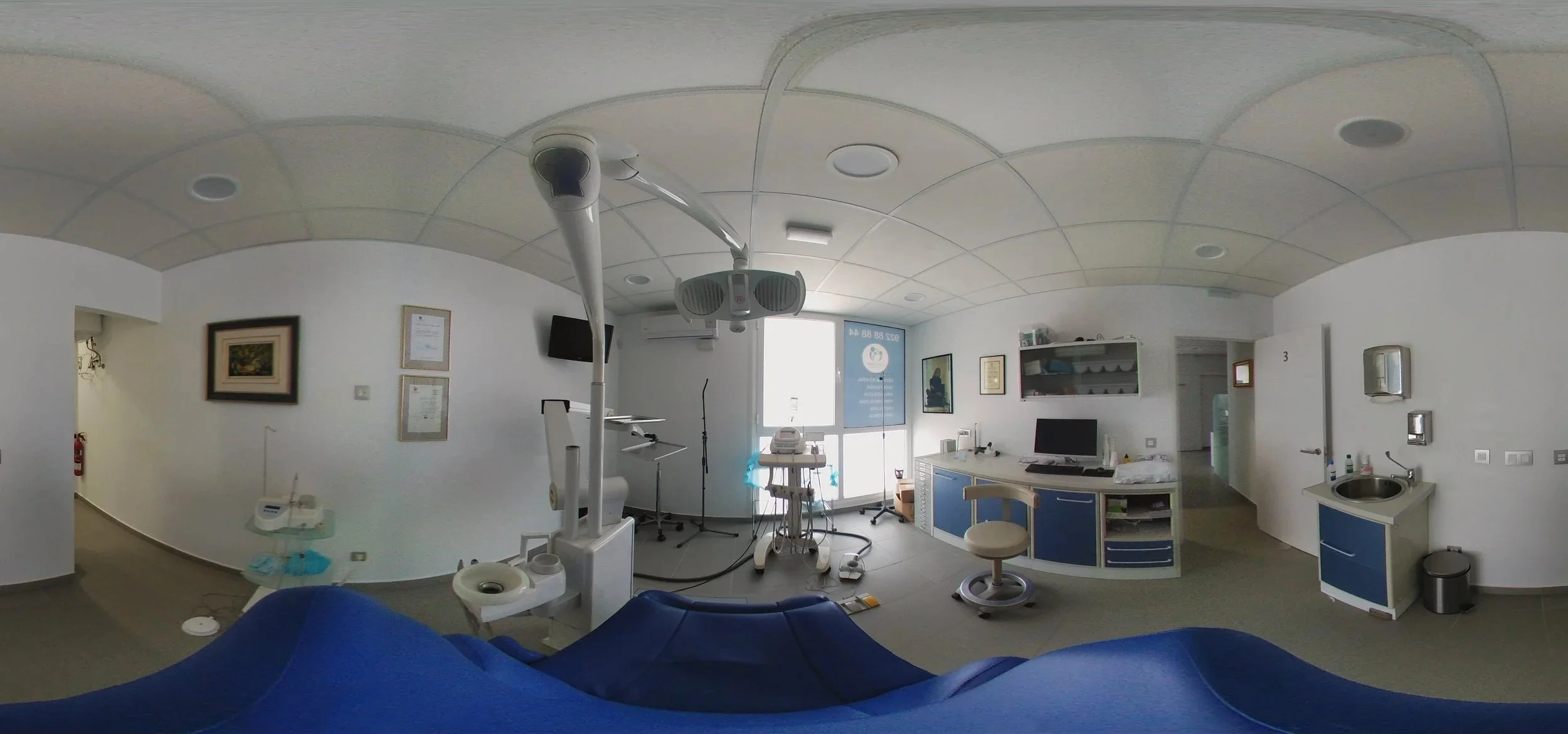 Vista a 360 gradi di una stanza medica o di un ambulatorio con attrezzature come un monitor, un dispositivo di risonanza, un laboratorio e un lavabo, con pareti bianche e arredi medici.