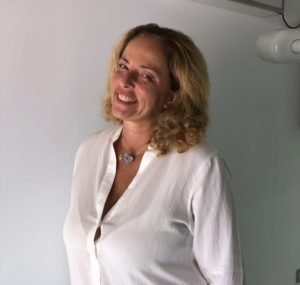Donna con capelli riccioli biondi che sorride, indossa una camicia bianca