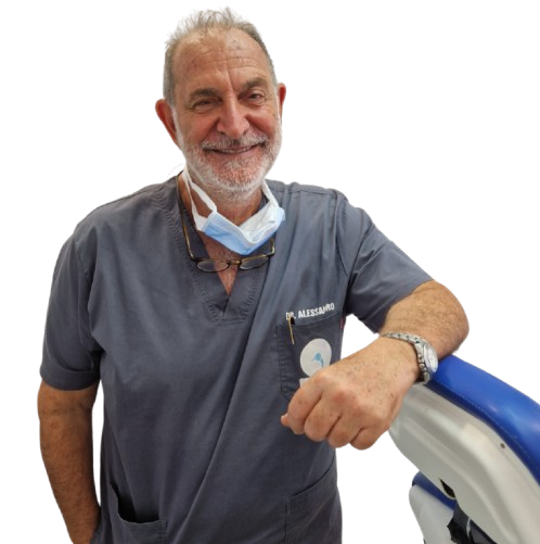 Uomo anziano sorridente indossa una divisa da medico e una mascherina abbassata, appoggiato a un apparecchio medicale.