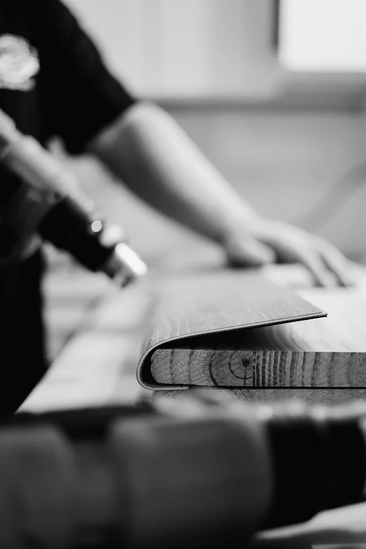 Close-up of a rolling pin on a wooden countertop, with a person in the background using a spray bottle.