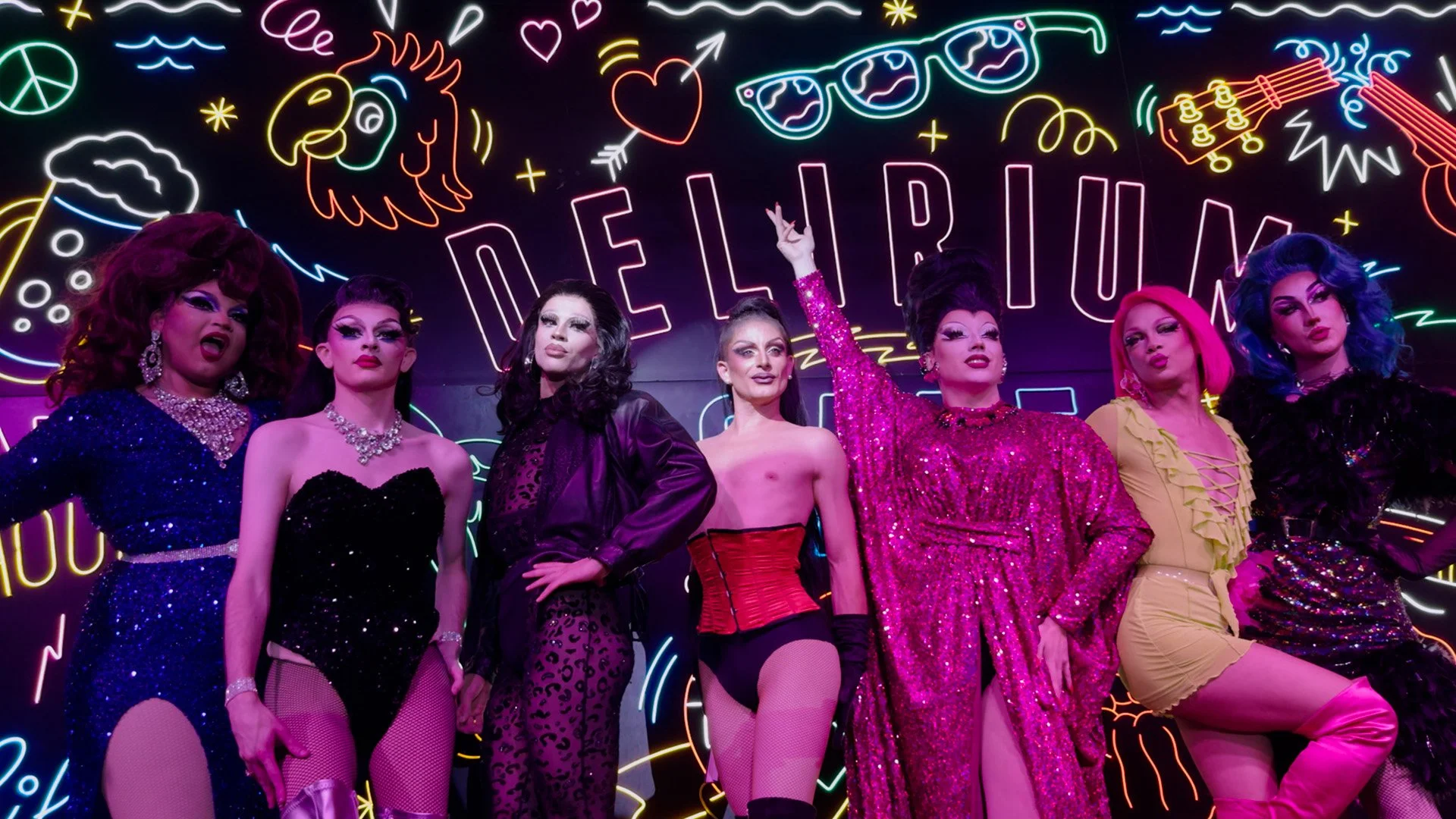 La troupe complète des artistes et guests de La Nuit Drag posant sur scène devant le néon du Delirium Cafe.