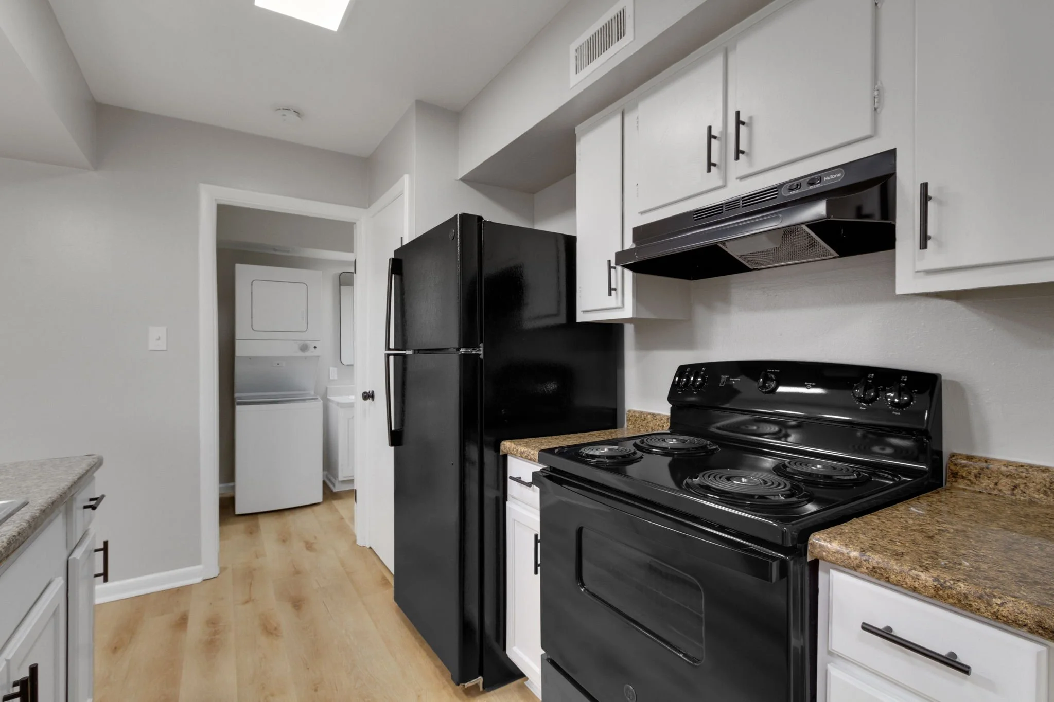 Kitchen with black refrigerator, black stove, white cabinets, granite countertops, and a laundry area with a washer and dryer in the background.