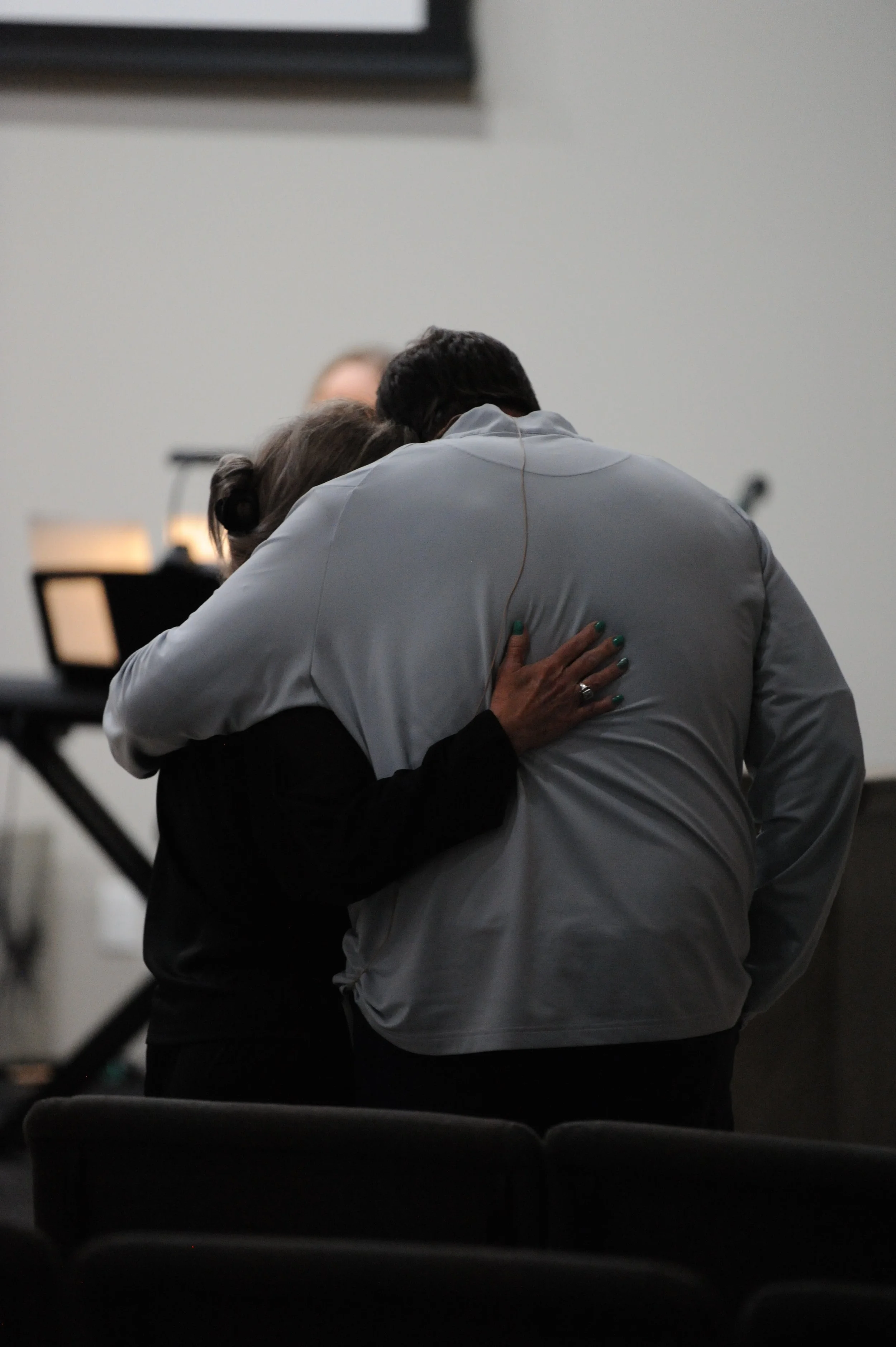 Two people hugging in a room, with a keyboard and a screen in the background.