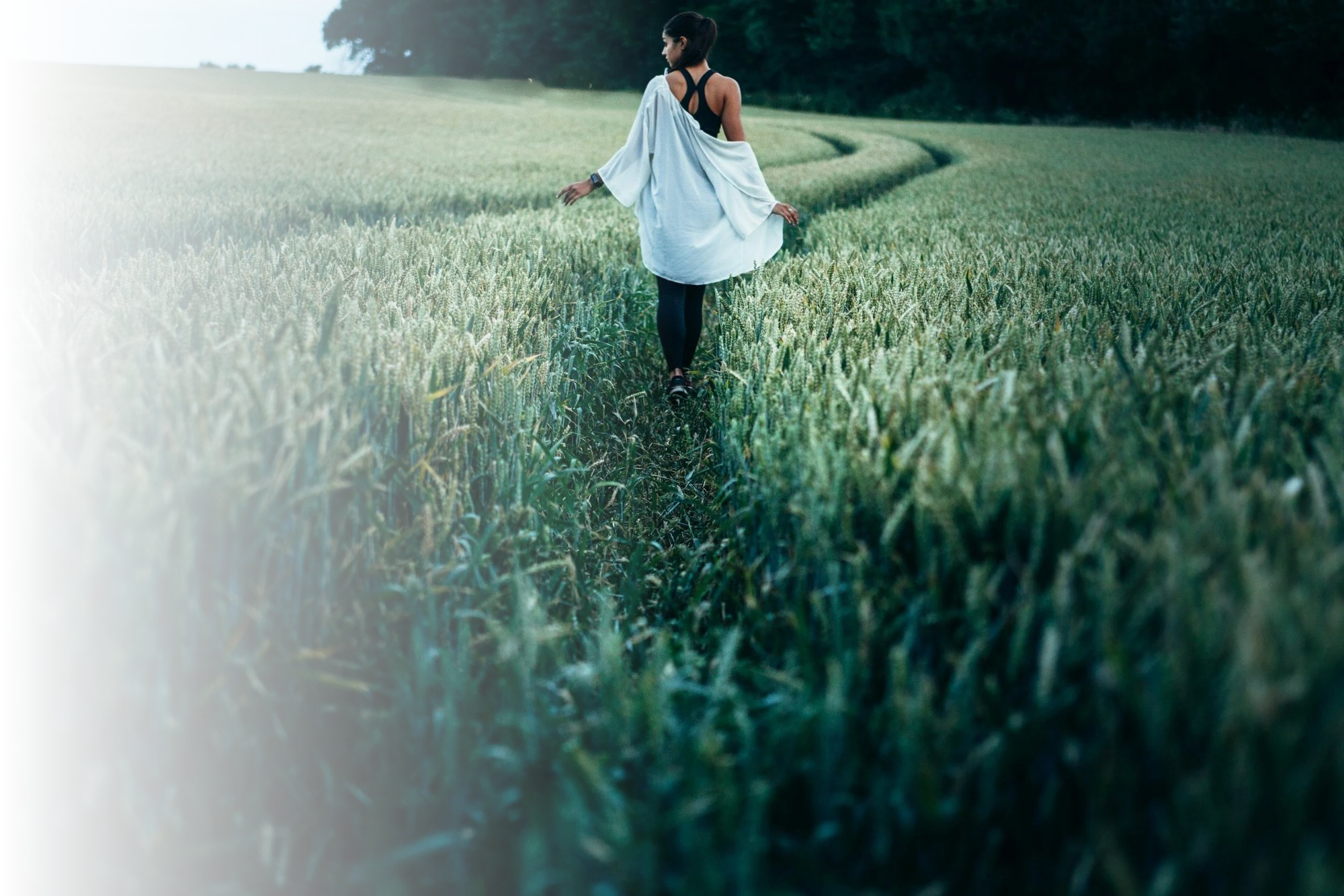 A woman walking through a lush green wheat field during the daytime.