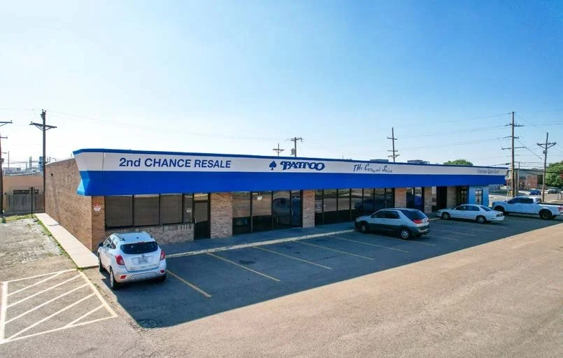 A single-story commercial building with a blue awning with several parked cars in front.