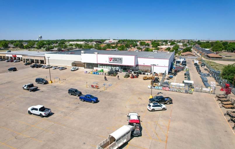 View of Tractor Supply Co. store in a parking lot with several parked cars and few people, clear blue sky.