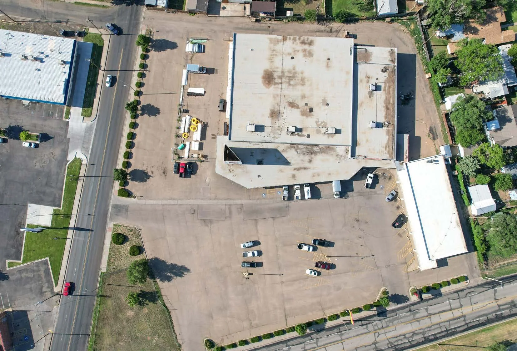 Aerial view of a commercial building with parking lot, surrounded by streets, trees, and residential homes.