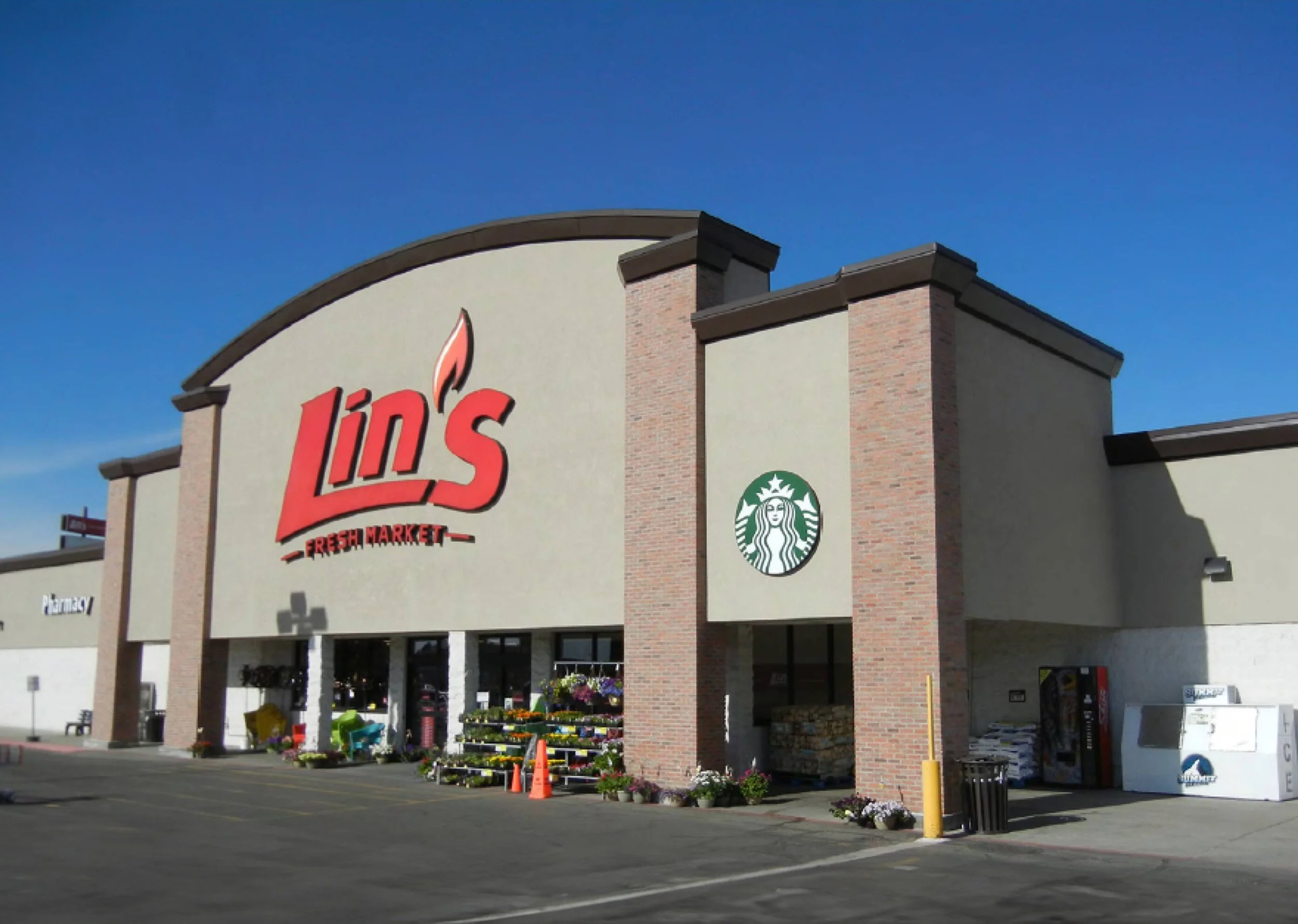 Exterior of a grocery store named Lin's Fresh Market with Starbucks logo on the side, in a parking lot under a clear blue sky.