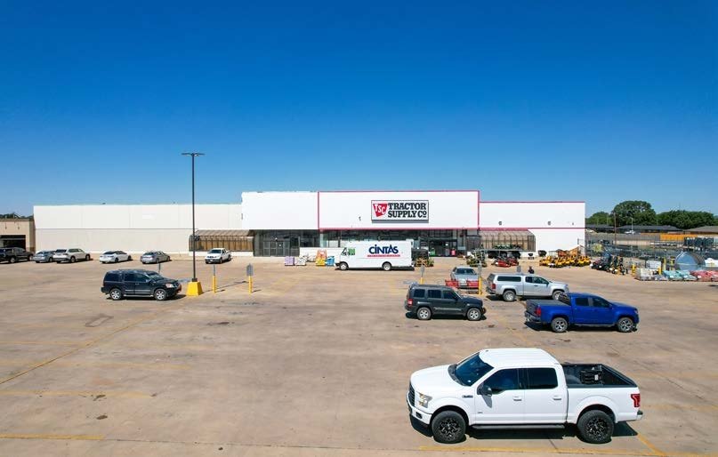 Large parking lot in front of Tractor Supply Co. store, with several parked vehicles including pickup trucks and SUVs, under a clear blue sky.