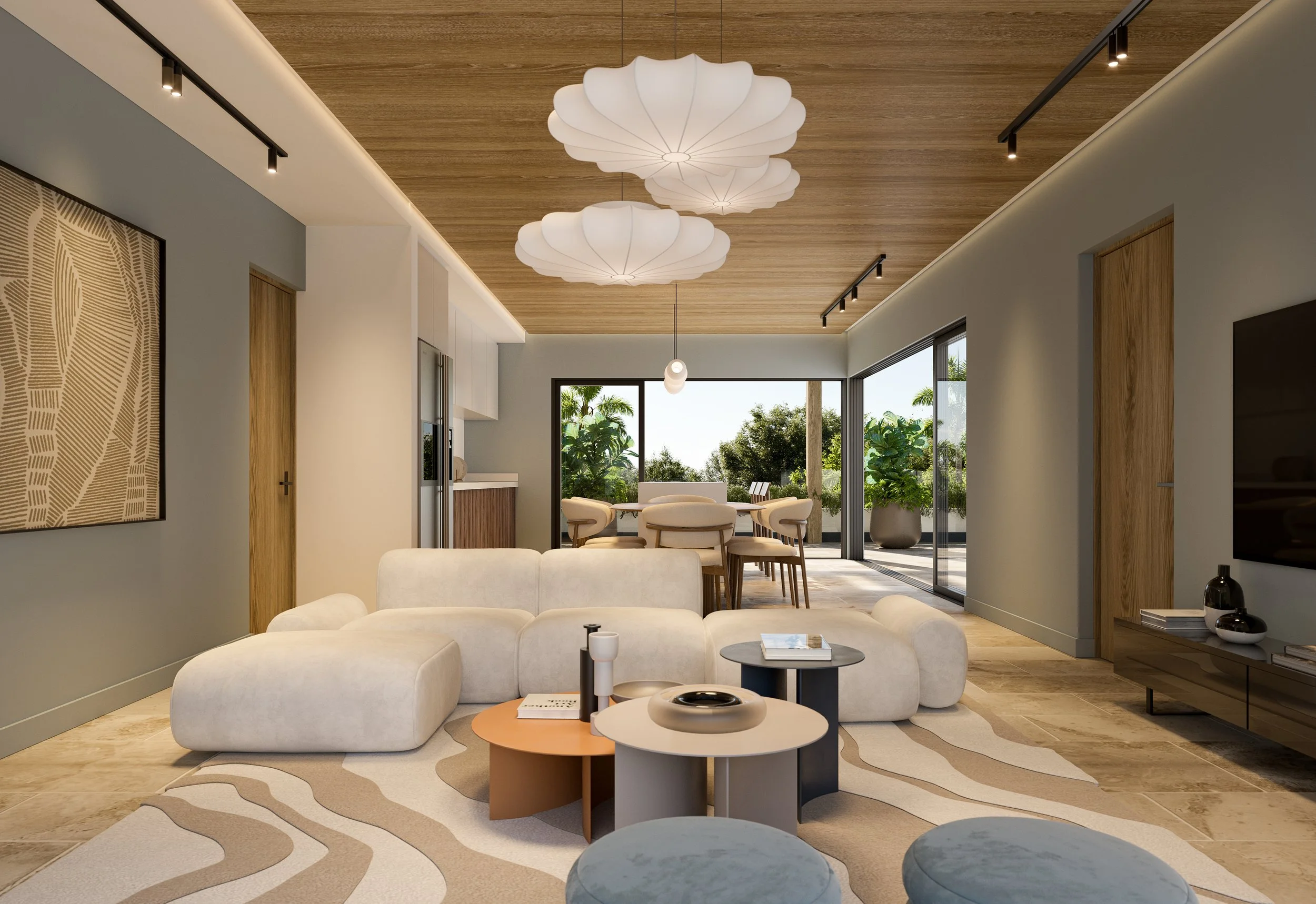 Living room with white sectional sofa, round coffee tables, and a patterned area rug. In the background, a dining area with a table and cushioned chairs, large sliding glass doors leading to an outdoor patio with potted plants, and modern pendant lig