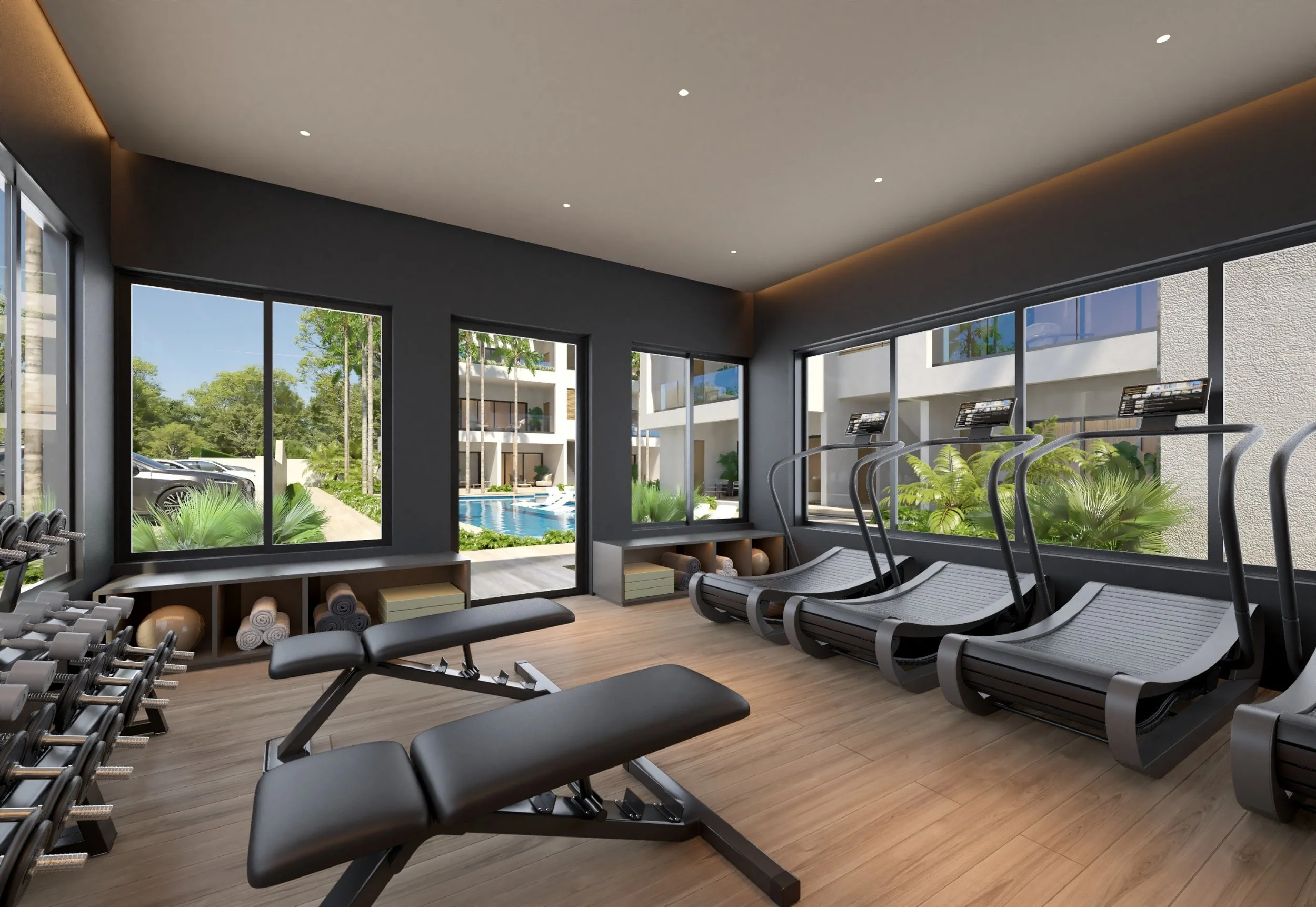 Interior view of a modern fitness room with treadmills, a weight bench, and free weights, overlooking an outdoor pool through large windows.