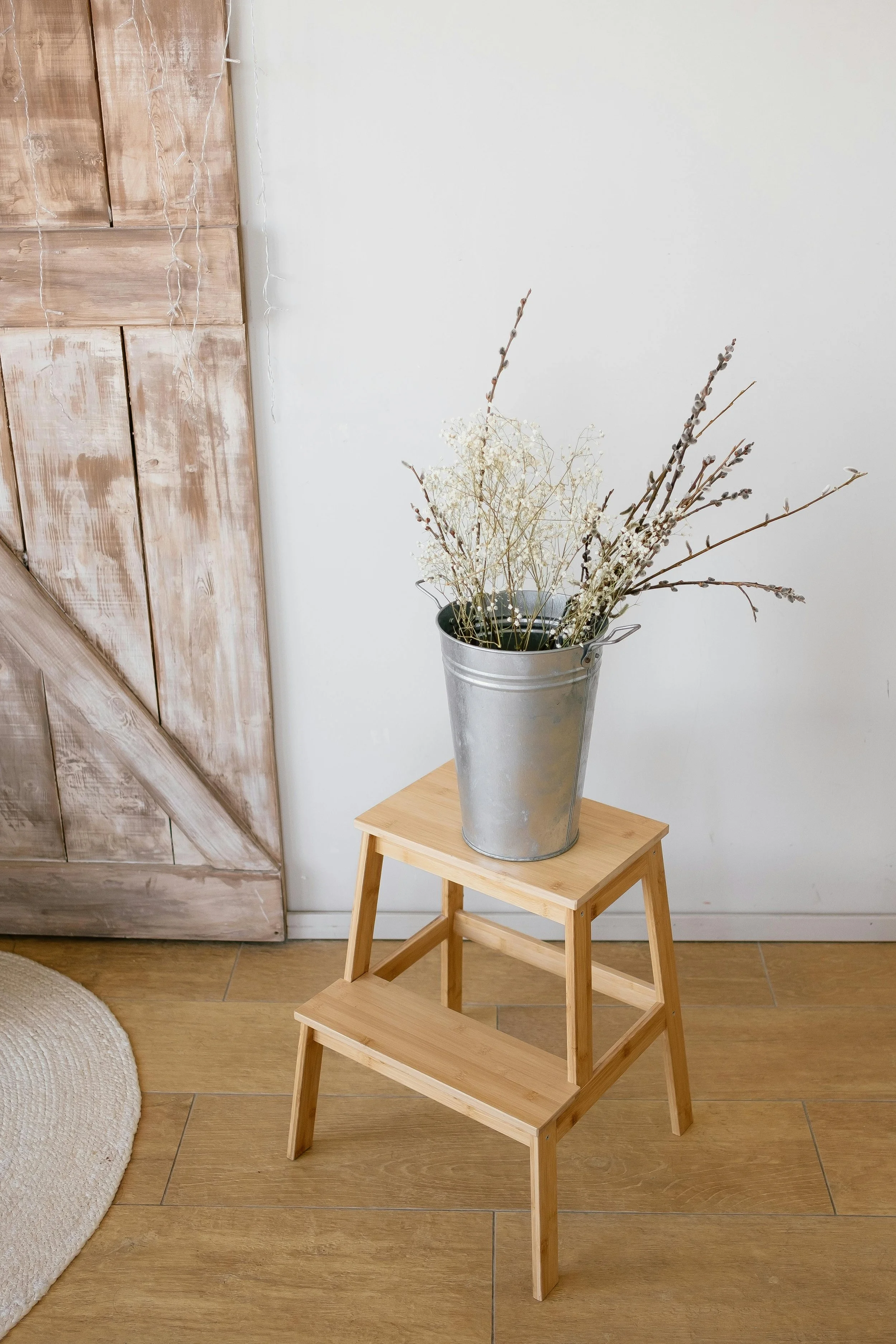 Two-step wooden stool signifying I-CBT's step-by-step approach with dried grass in tin canister on top and wooden door in background with rug off to side.
