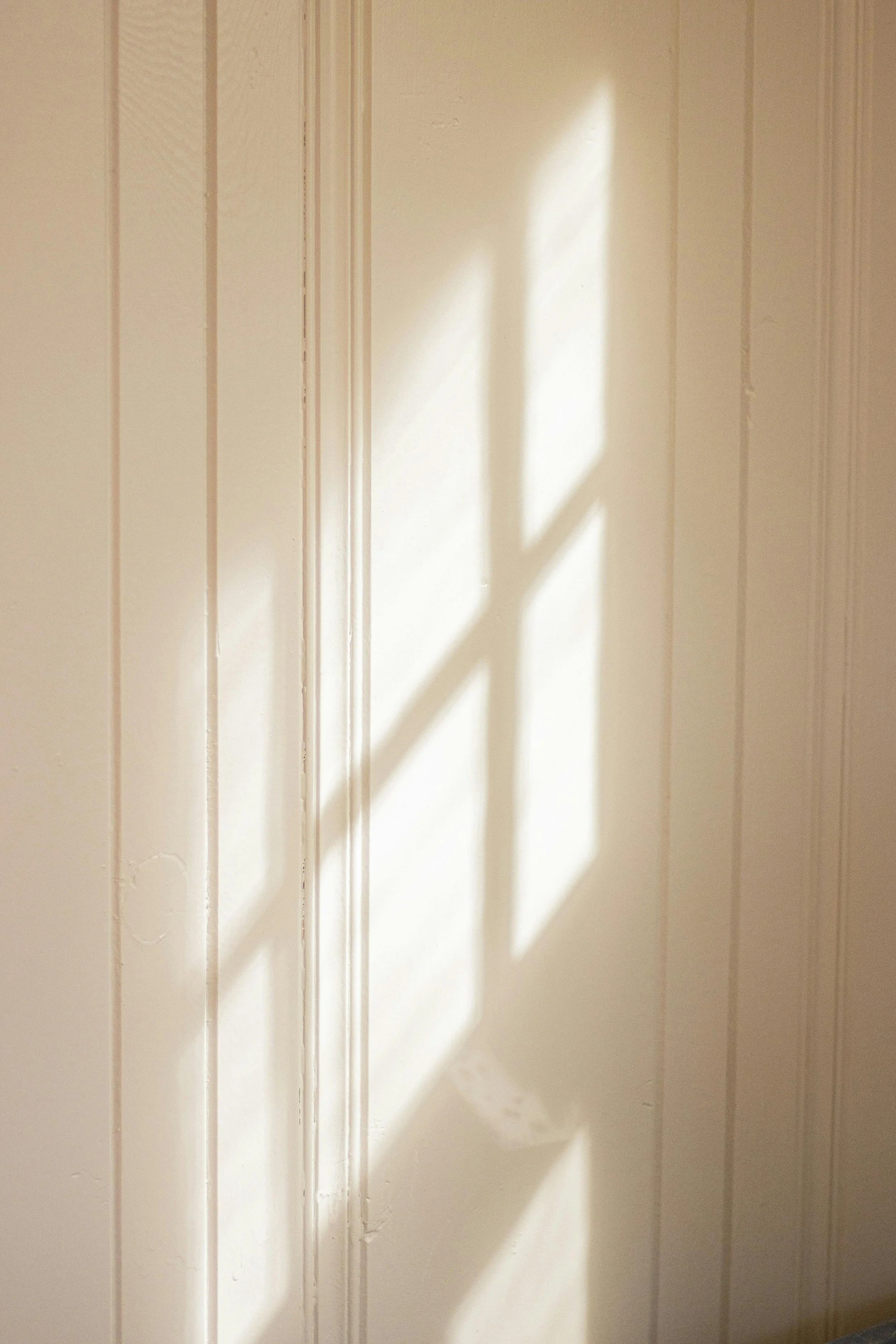 Bright light shining from a window onto a white shiplap wall.