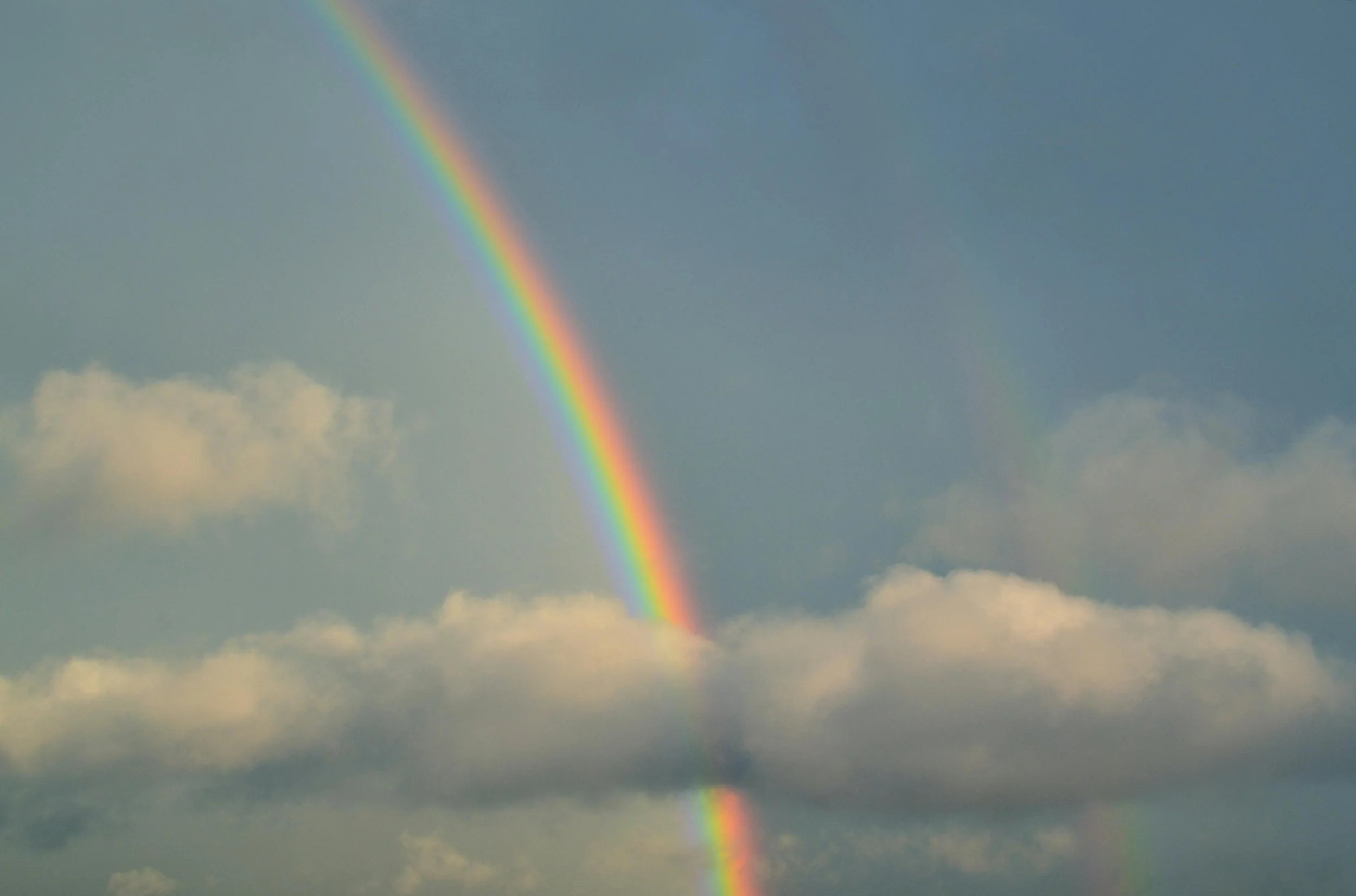 Rainbow arcing through clouds into a blue sky.