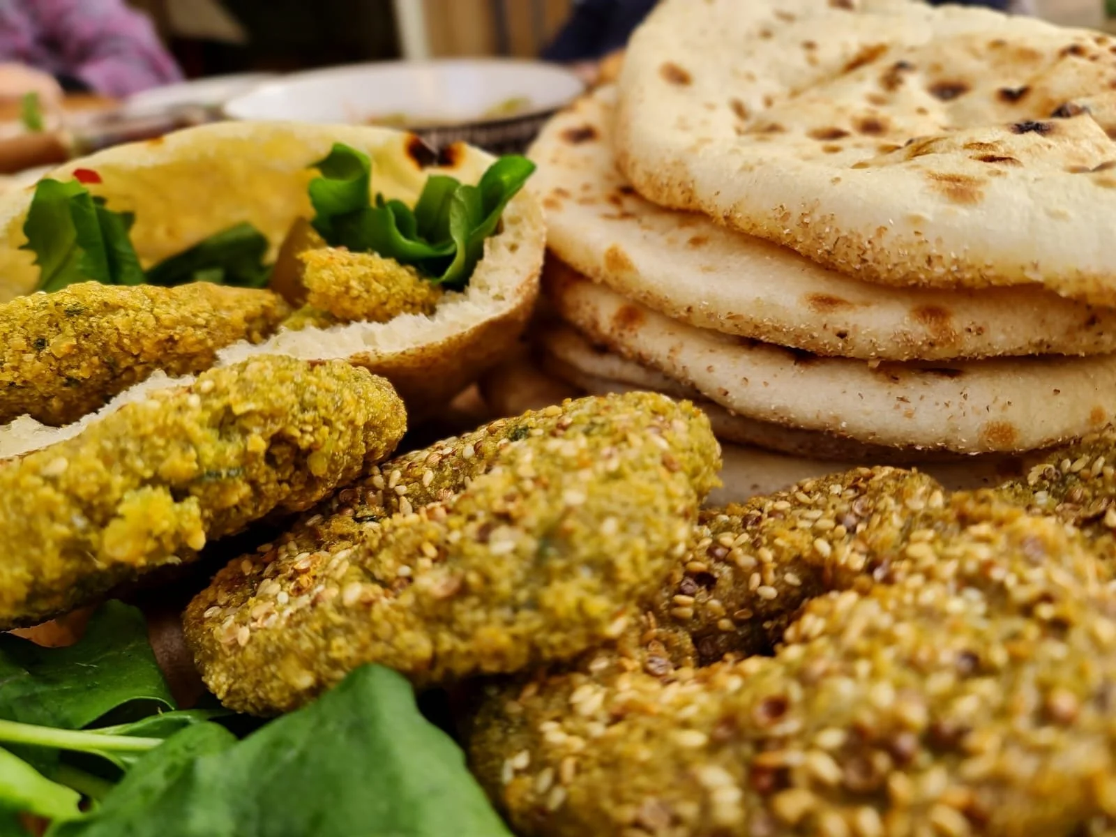 Close-up of falafel chips, Egyptian baladi bread, and a small bowl of hummus with green herbs on a plate.