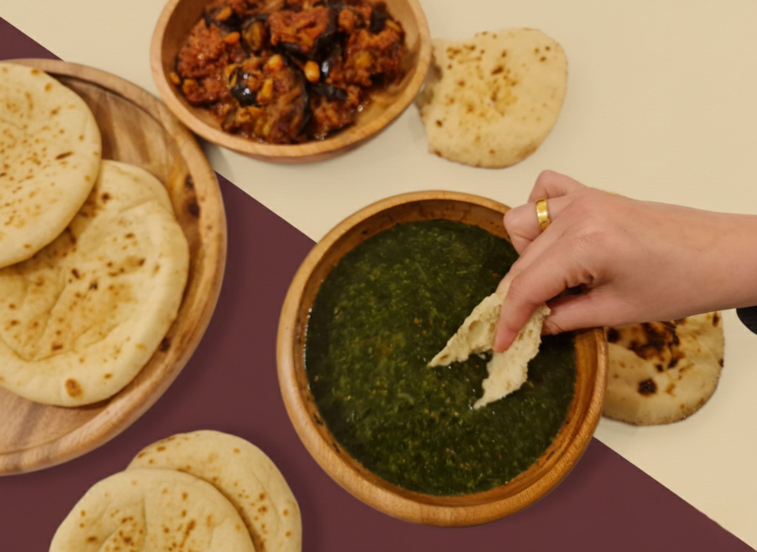 A person dipping Egyptian baladi flatbread into a bowl of green sauce, with other Egyptian baladi flatbreads, a bowl of vegetable stew, and more Egyptian baladi flatbreads on the table.