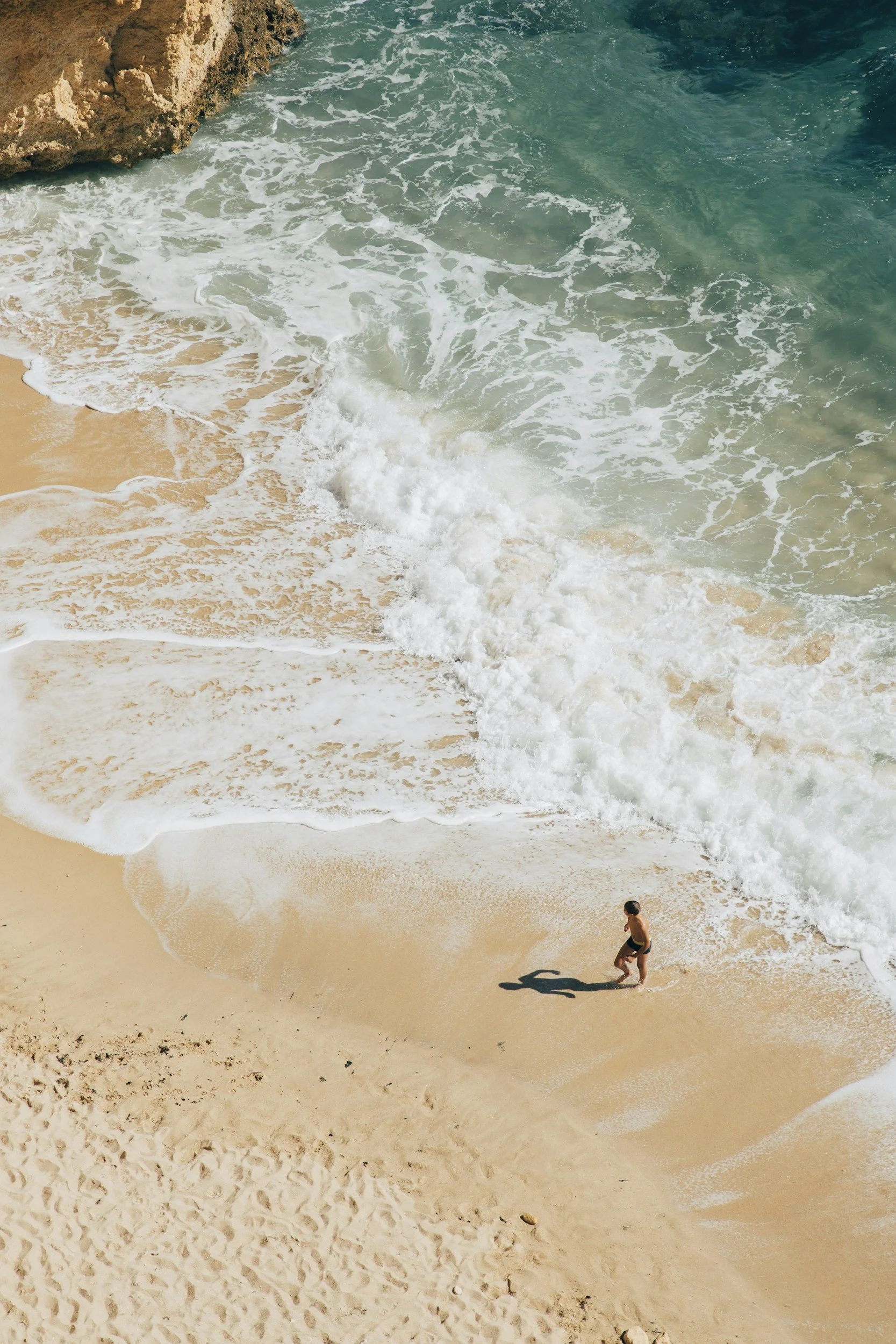 A person walking along the sandy shore of a beach with waves crashing onto the sand.
