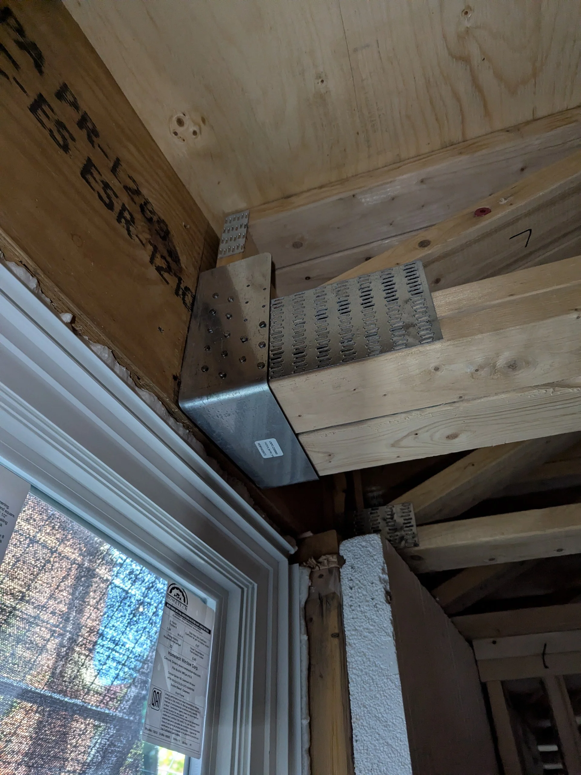 Construction framing around a window with metal support brackets and wood studs.