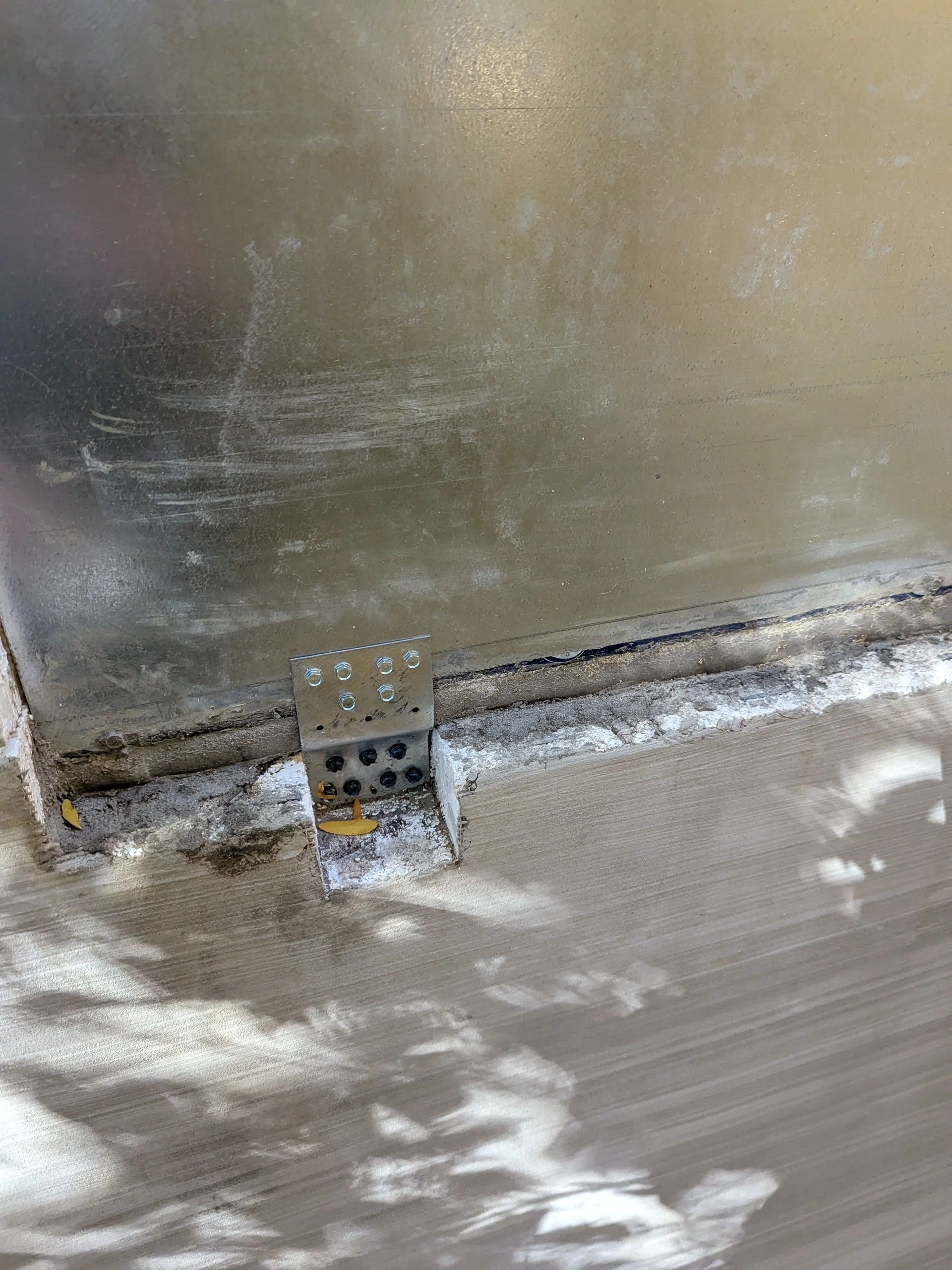 Close-up of a metal bracket securing a wall to a flooring surface, with some dust and debris around it.