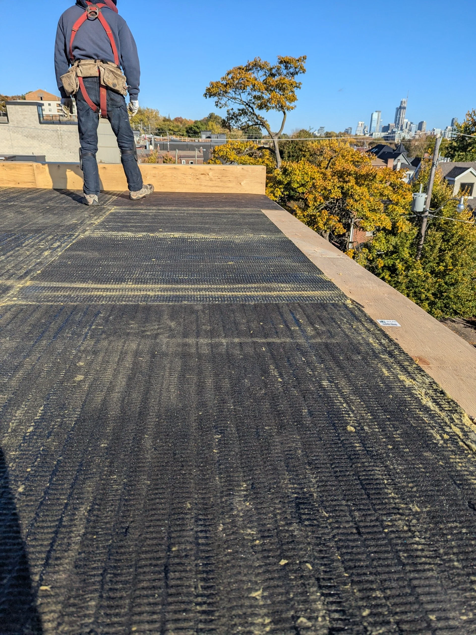 Construction worker standing on a rooftop at a building site with city skyline in the background during daytime.
